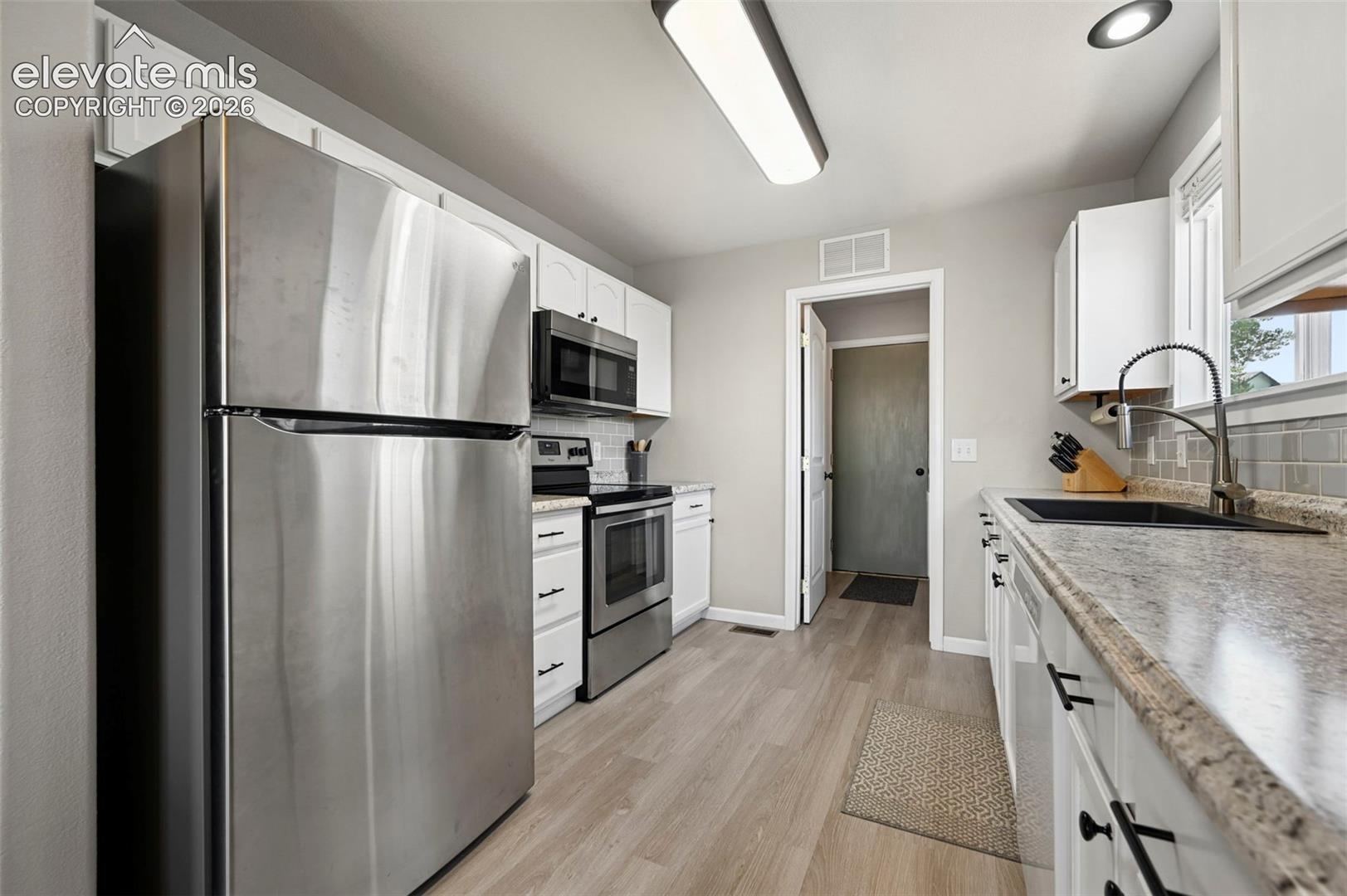Kitchen featuring white cabinetry with matte black hardware, stainless steel appliances, a black under-mount sink with a high-arch faucet, and wood-finish flooring