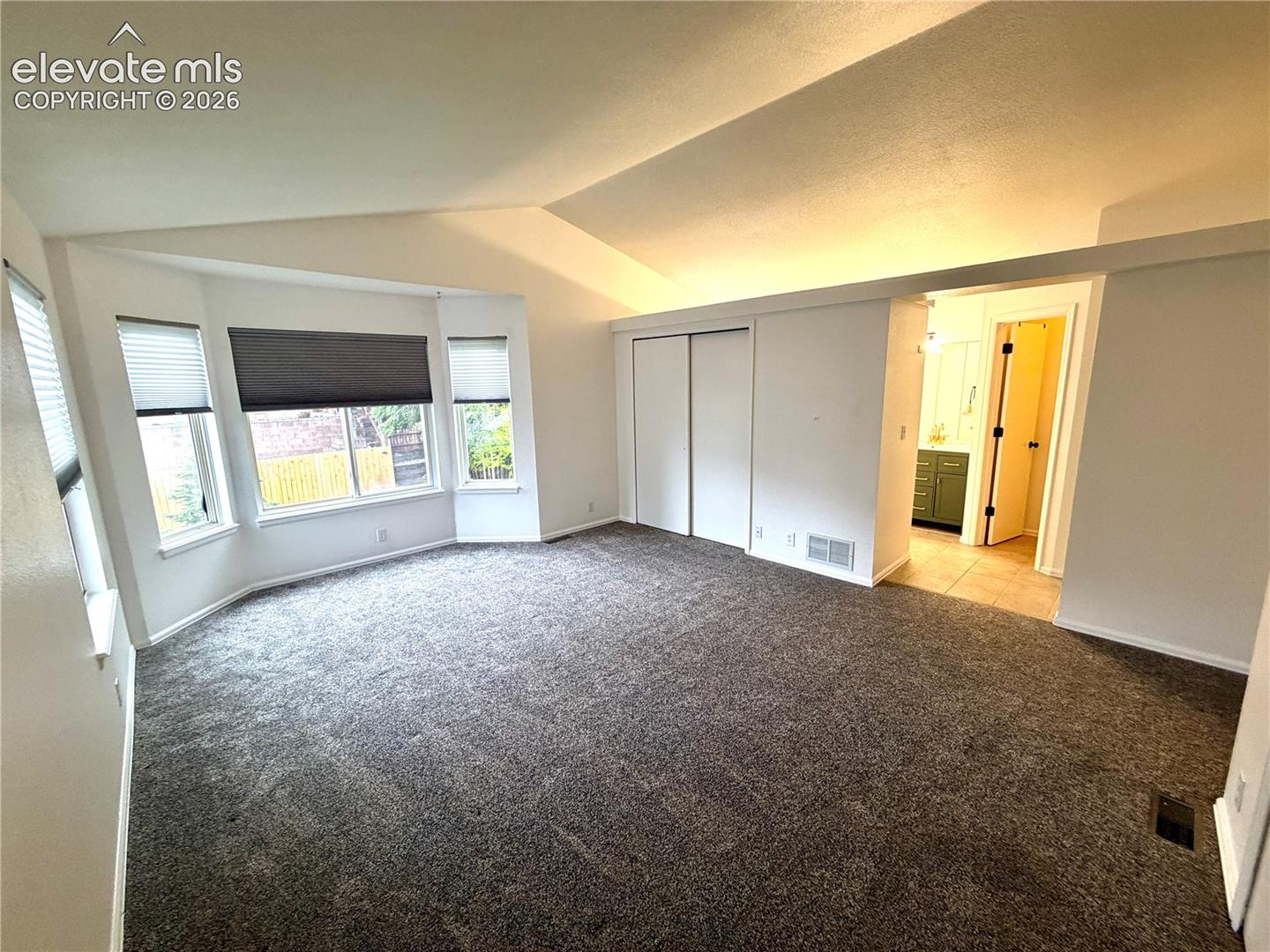 Carpeted room featuring a bay window with blinds, vaulted ceiling, and sliding closet doors