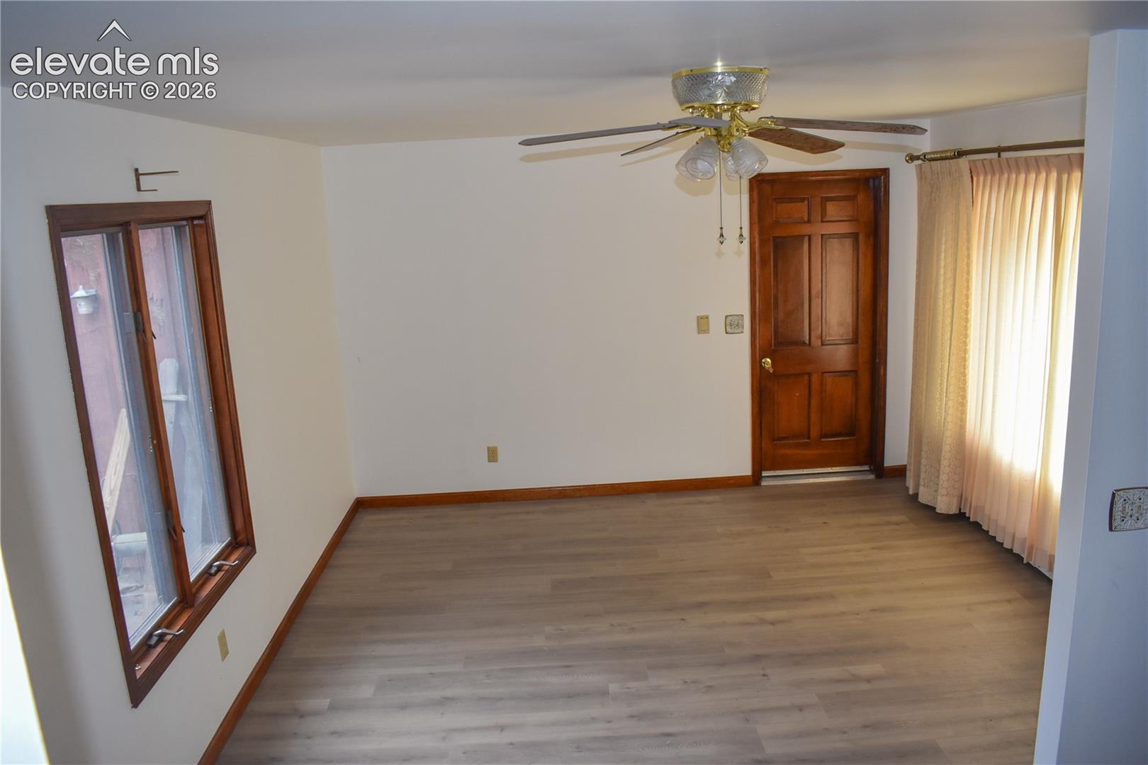 Light wood-finish flooring, wood trim, white walls, and a ceiling fan with integrated lighting