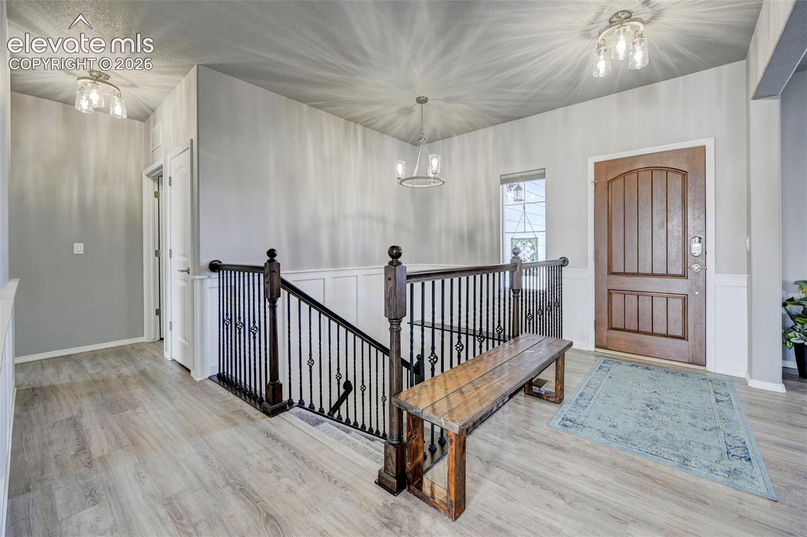 Entryway featuring wood-finish flooring, wainscoting, and a wood entry door with an arched top panel