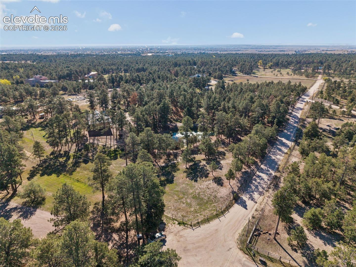 Aerial perspective featuring expansive acreage, mature evergreen trees, and direct access to a secondary road