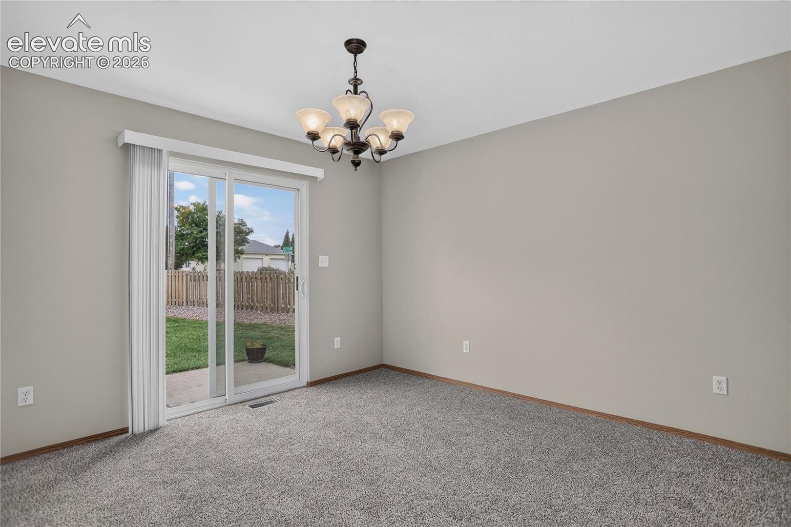 Sliding glass door, light gray wall paint, dark wood-finish trim, ceiling-mounted chandelier, and gray carpeting