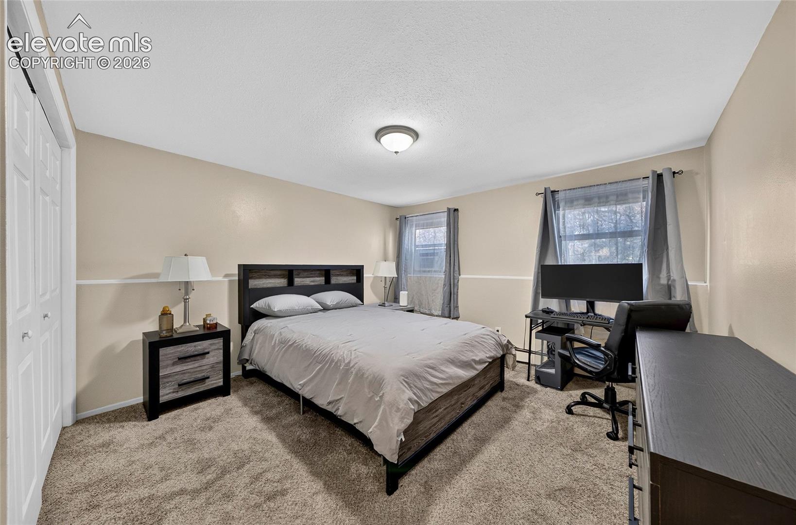 Neutral-toned room featuring carpeting, two windows with window treatments, and a closet with bifold doors