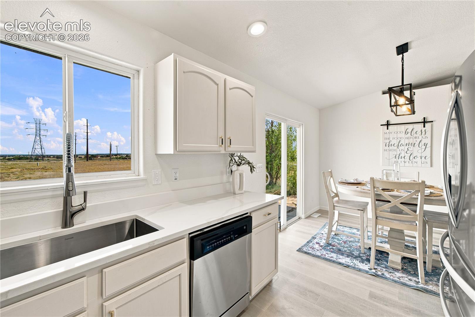 Kitchen featuring a stainless steel undermount sink, a pull-down faucet, a built-in dishwasher, white cabinetry, and light-toned countertops