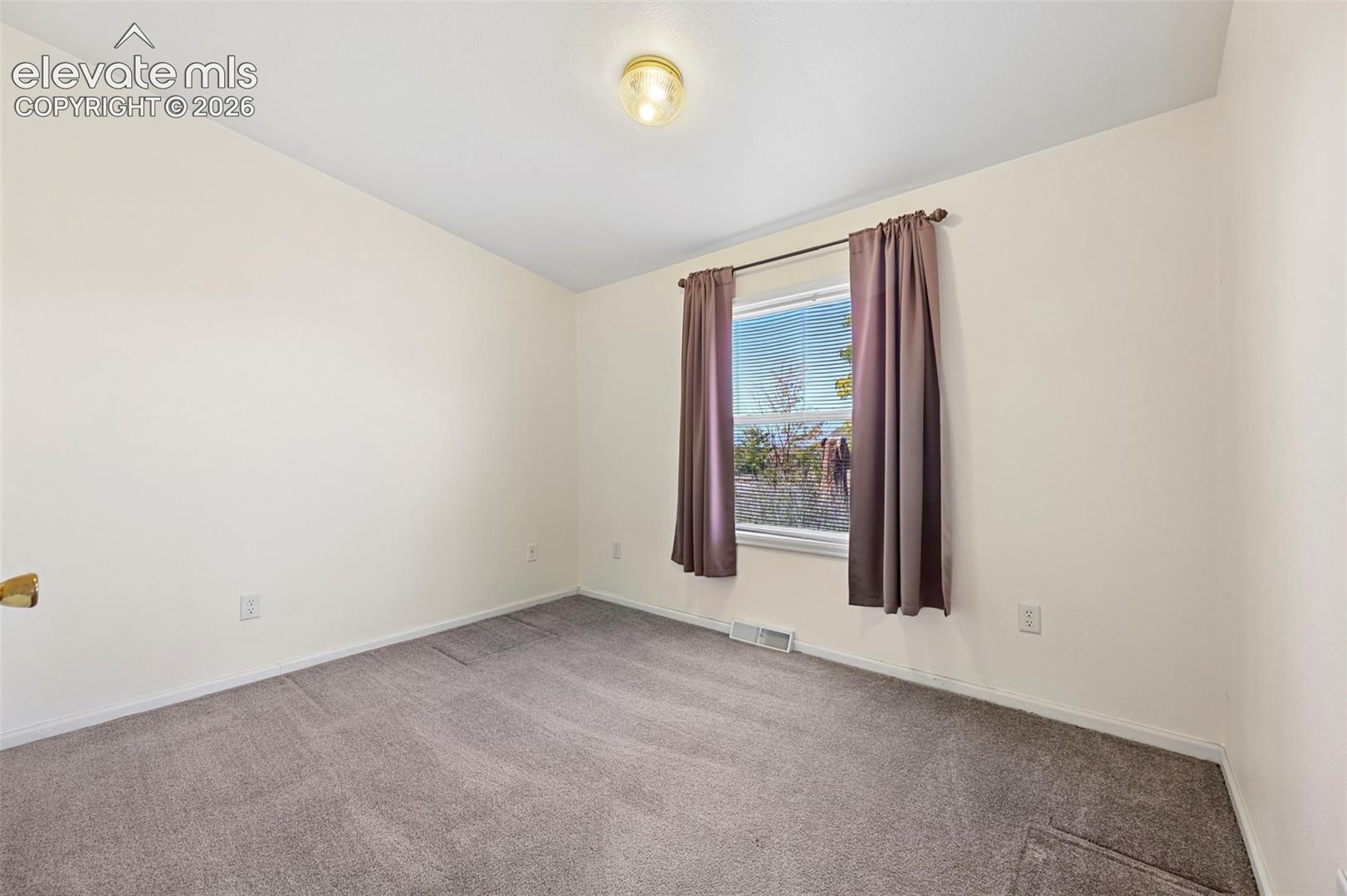 Neutral-toned interior room featuring wall-to-wall carpeting and a single-hung window with a polished metal rod