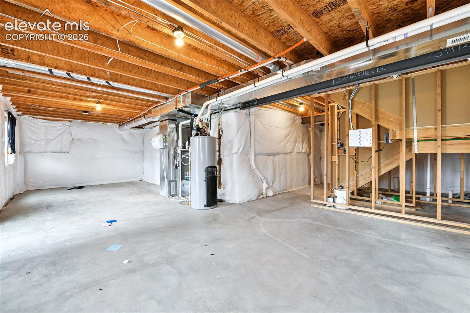 Unfinished lower level featuring exposed wood-joist ceiling, concrete flooring, insulated wall wrap, and integrated water heater