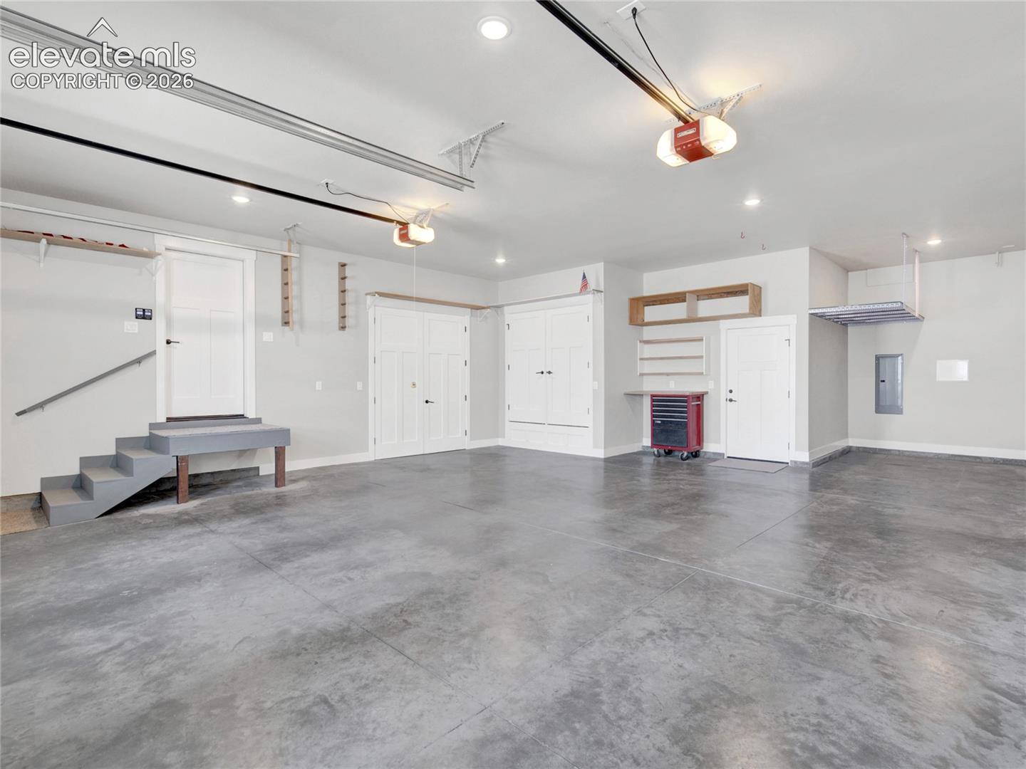 Spacious garage with durable concrete flooring, multiple overhead lighting fixtures, and a staircase for interior access