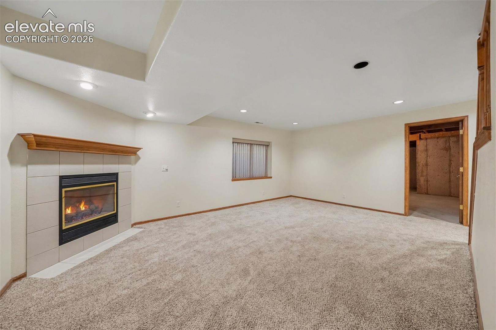 Carpeted room featuring a tile-surround fireplace with a wood mantel, recessed lighting, and a window with blinds
