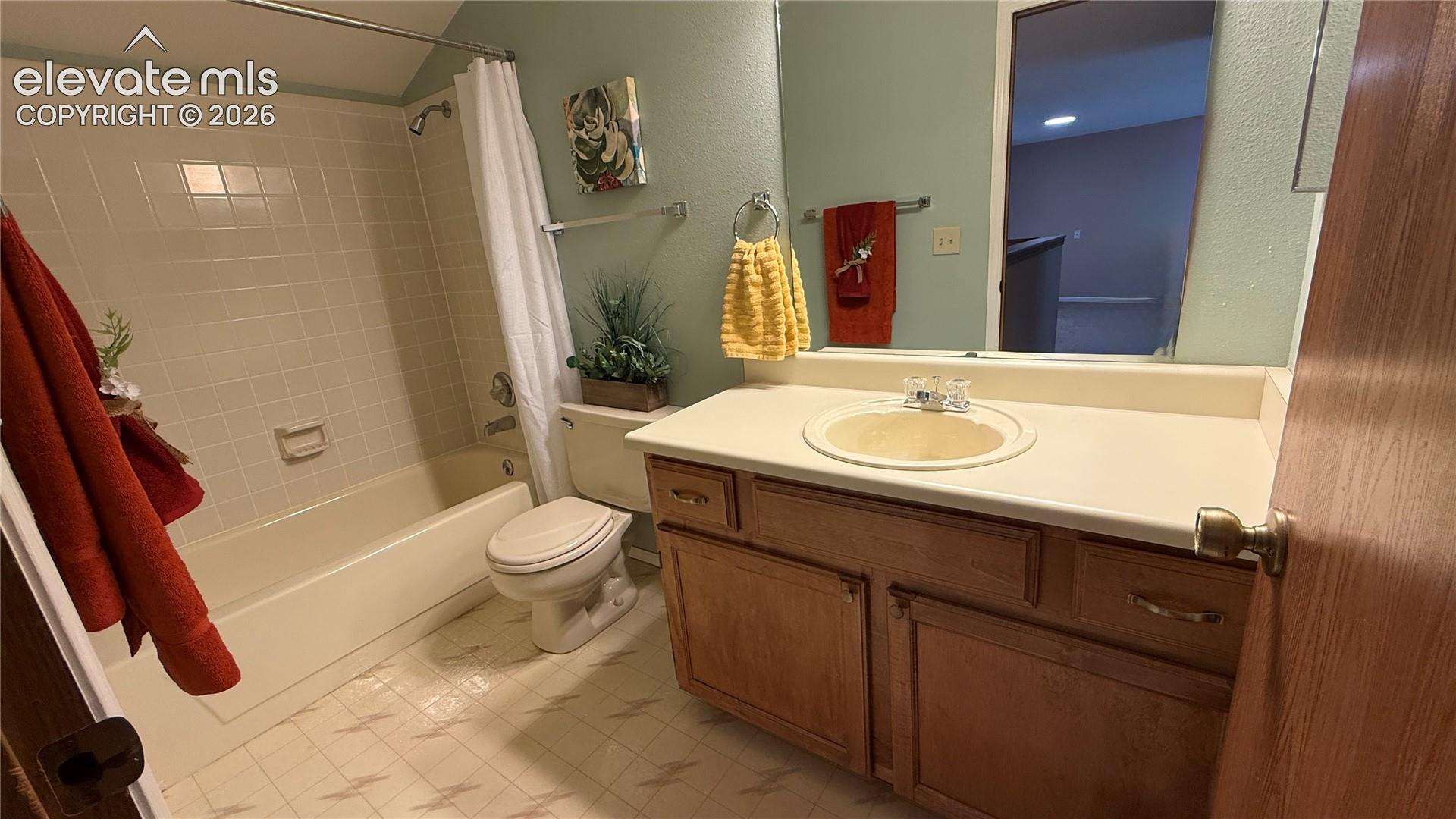Bathroom featuring a wood vanity with a lite colored countertop, an integrated sink, a tiled bathtub surround, and a large wall-mounted mirror