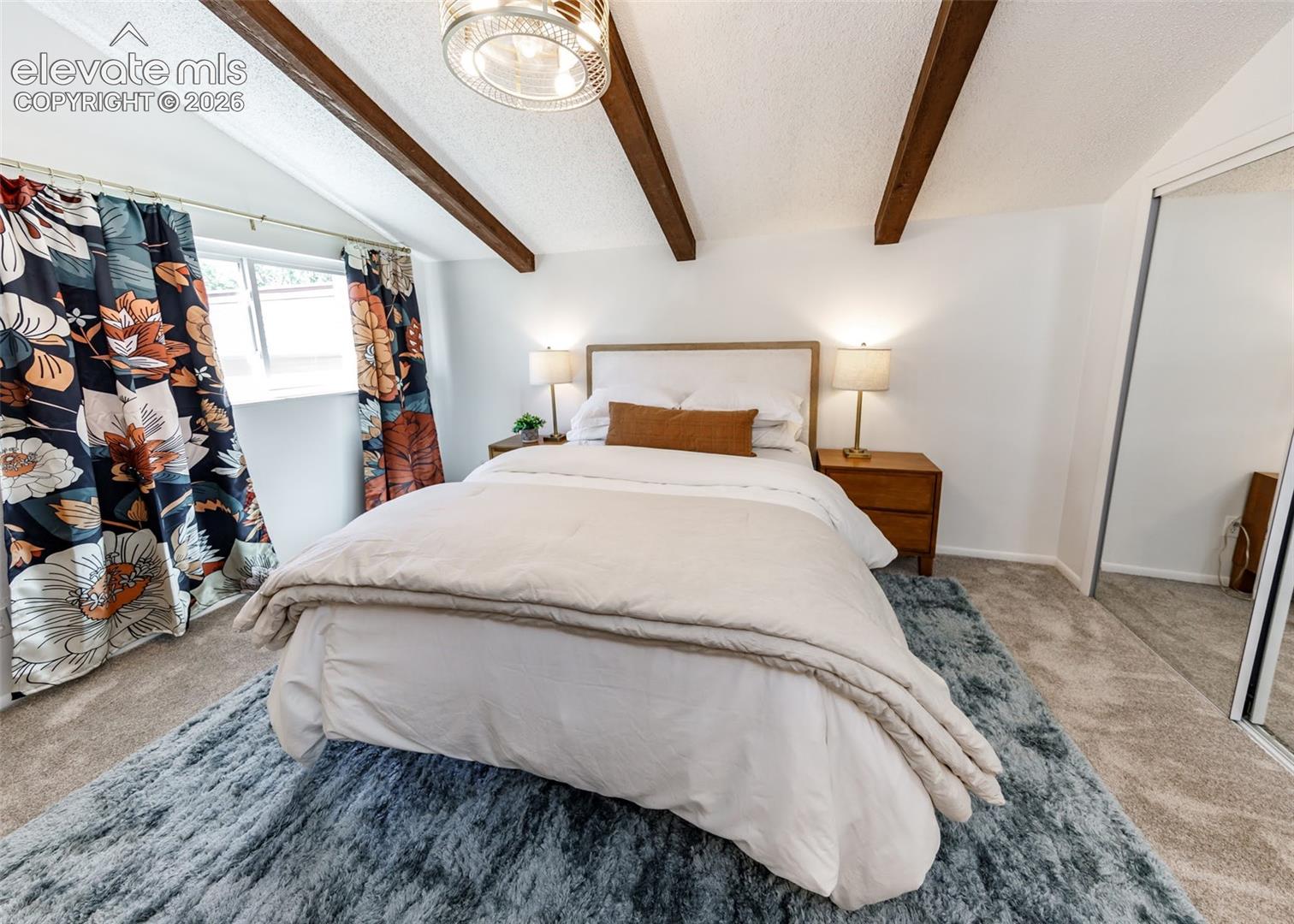 Vaulted ceiling featuring exposed wood-finish beams, wall-to-wall carpeting, and sliding mirrored closet doors