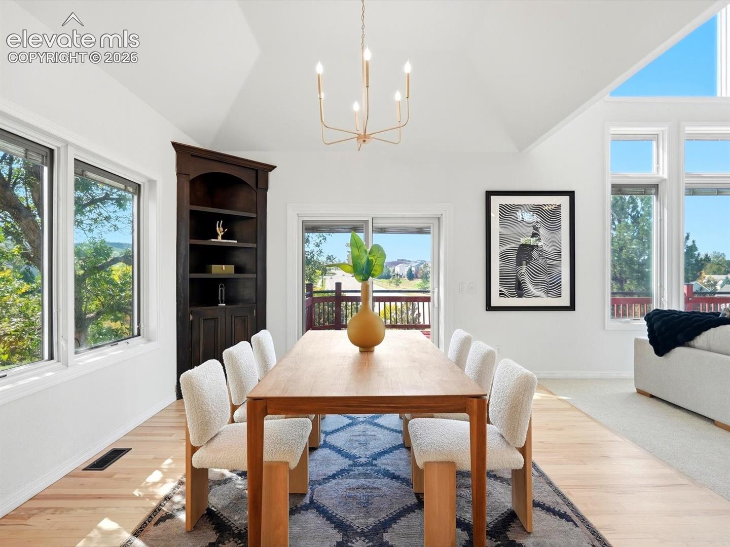 Vaulted ceilings, built-in corner cabinetry, large picture windows, sliding glass door, and a multi-arm chandelier