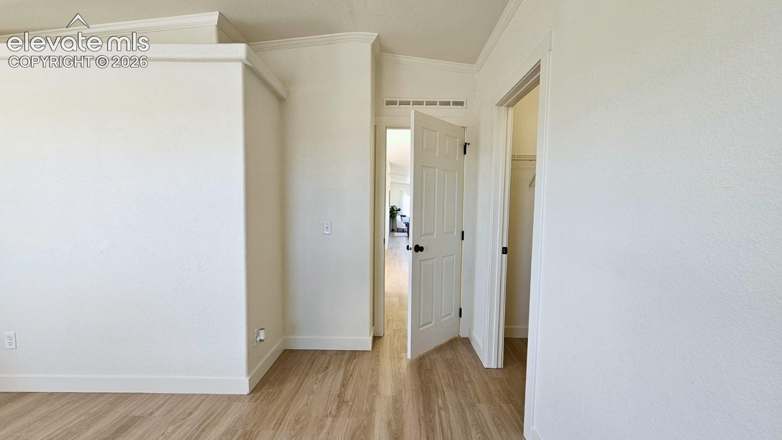 Interior space featuring light-toned wood-finish flooring, crisp white walls, crown molding, and two-panel interior doors