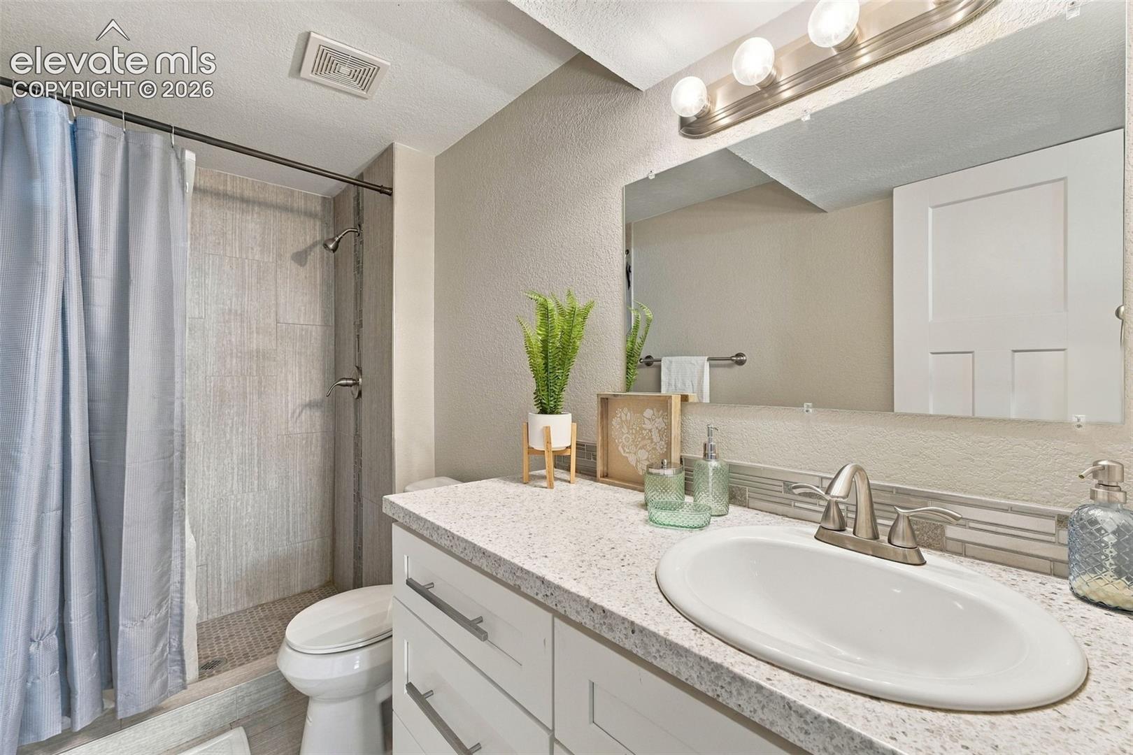 White vanity with brushed nickel hardware, speckled countertop, and an oval undermount sink