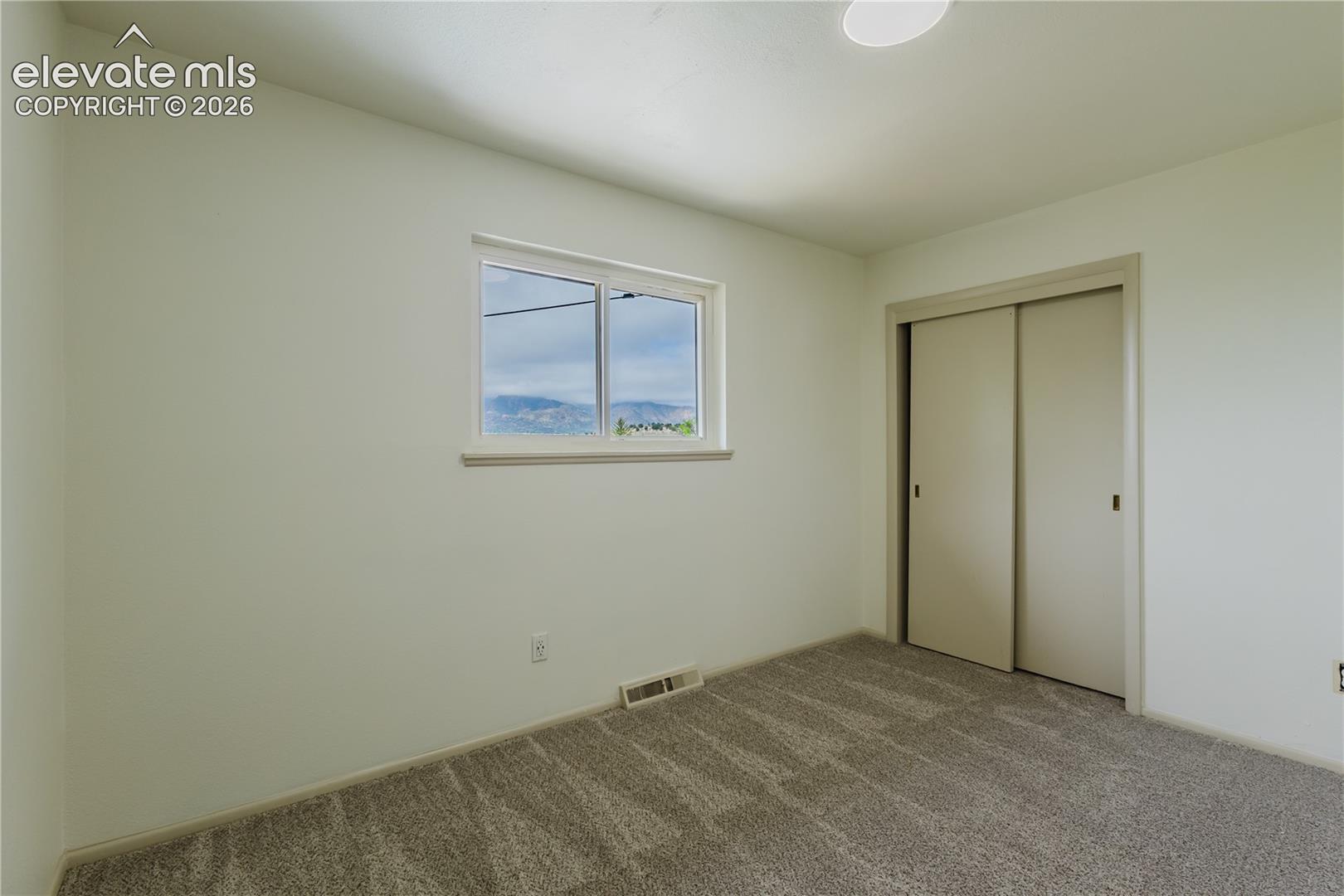 Neutral-toned room featuring a single window, carpet flooring, and a sliding closet door