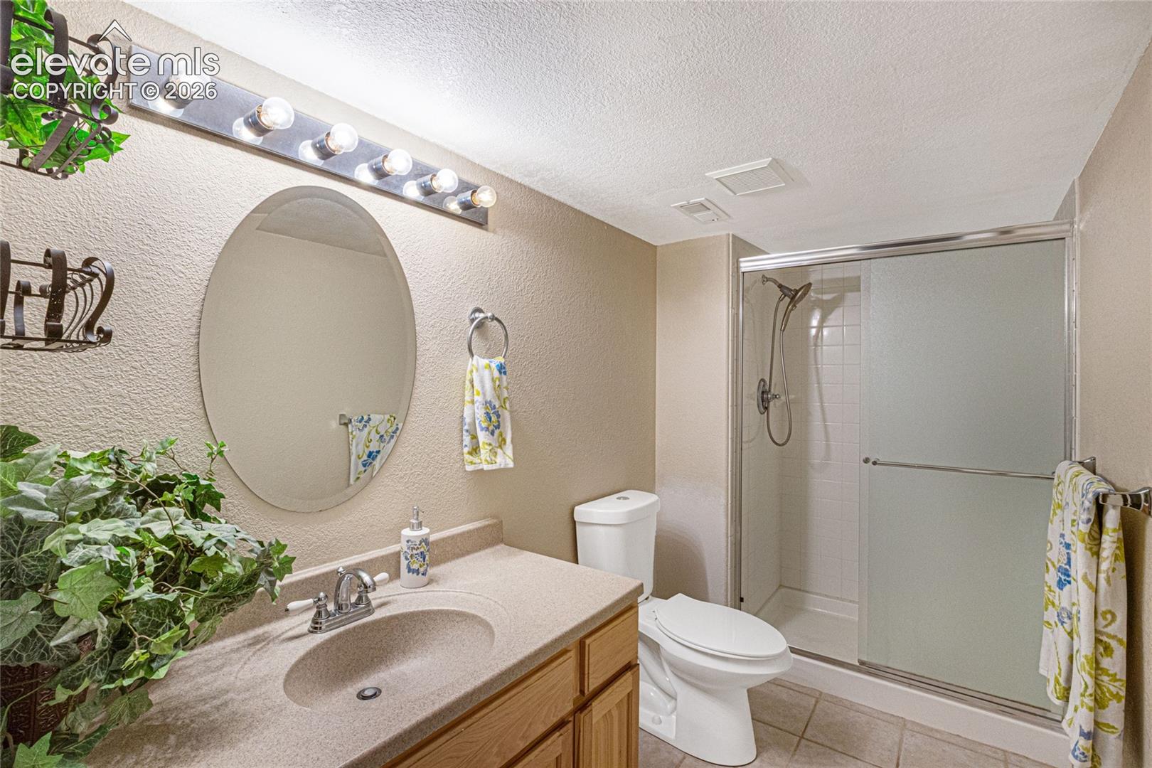Bathroom featuring an oval vanity mirror, wood-finish cabinetry, solid-surface integrated sink countertop, and a walk-in shower with sliding glass doors