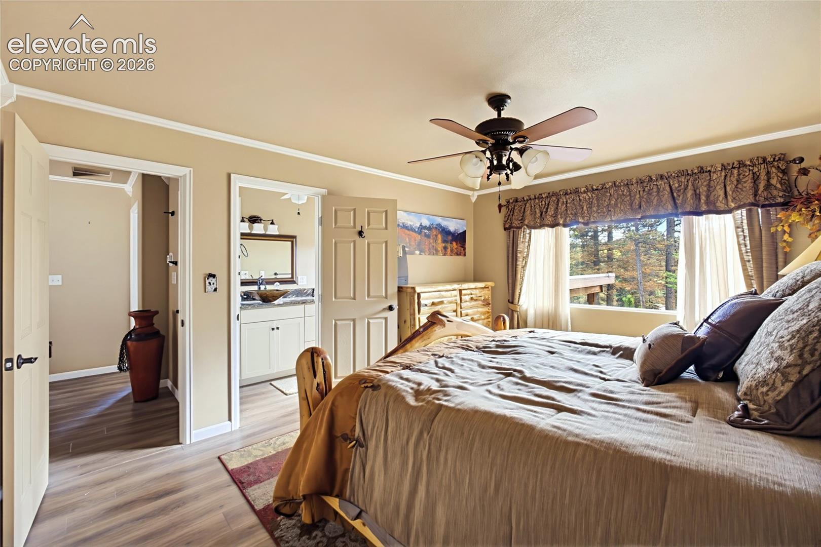 Wood-finish flooring, ceiling fan with integrated light fixture, and multi-pane window featuring exterior tree-line scenery