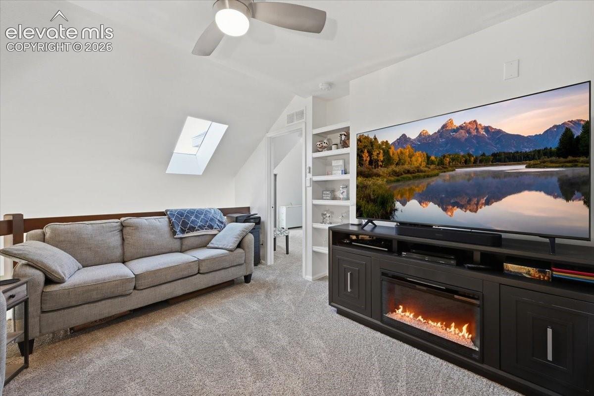 Sloped ceiling featuring a skylight, built-in shelving, carpeted flooring, and a ceiling fan with integrated lighting