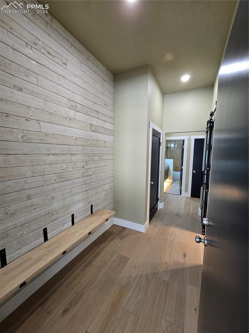 Corridor with light wood-type flooring, a barn door into laundry, and wooden walls