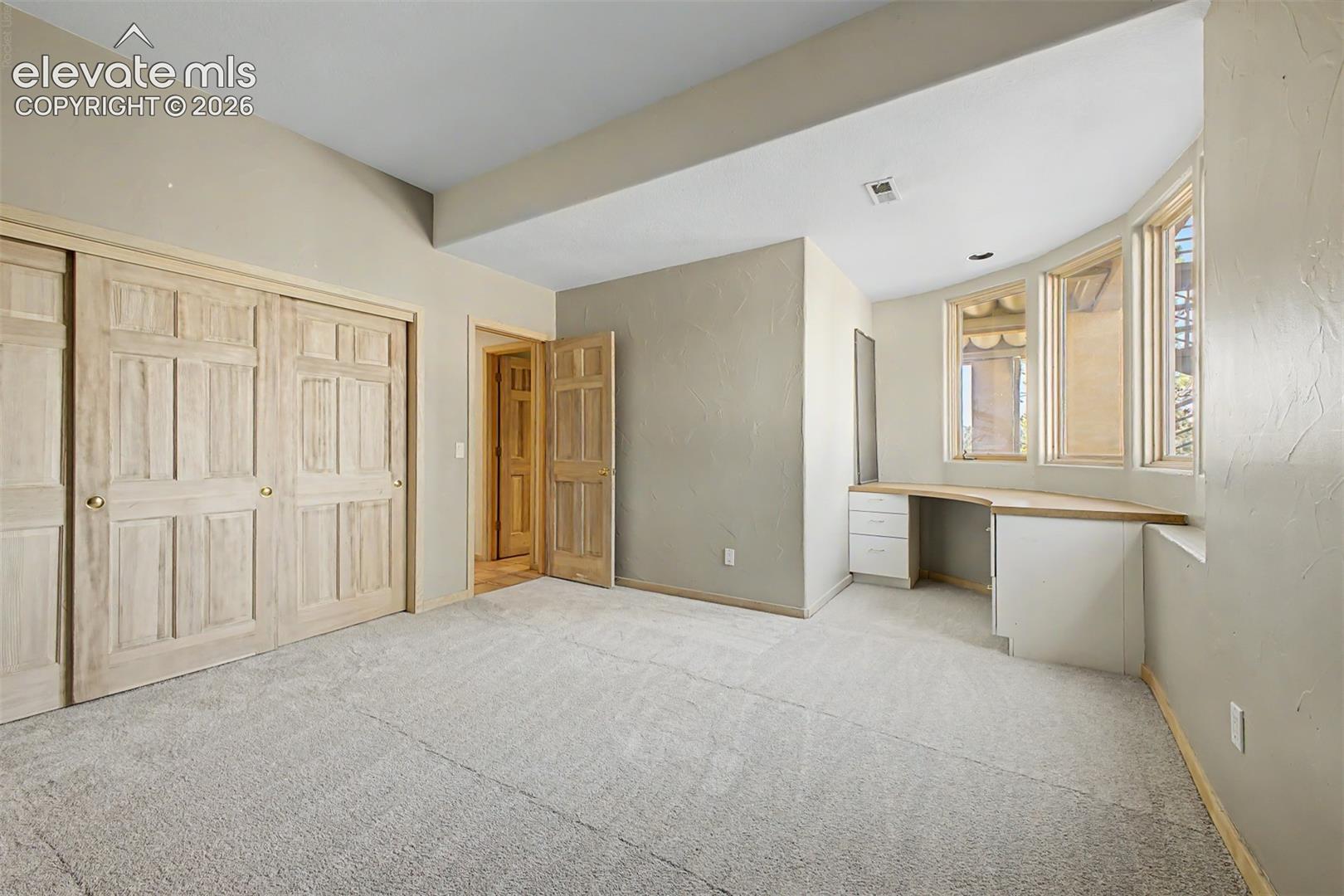 Built-in desk with a curved window wall, neutral carpeting, and panel-style closet doors