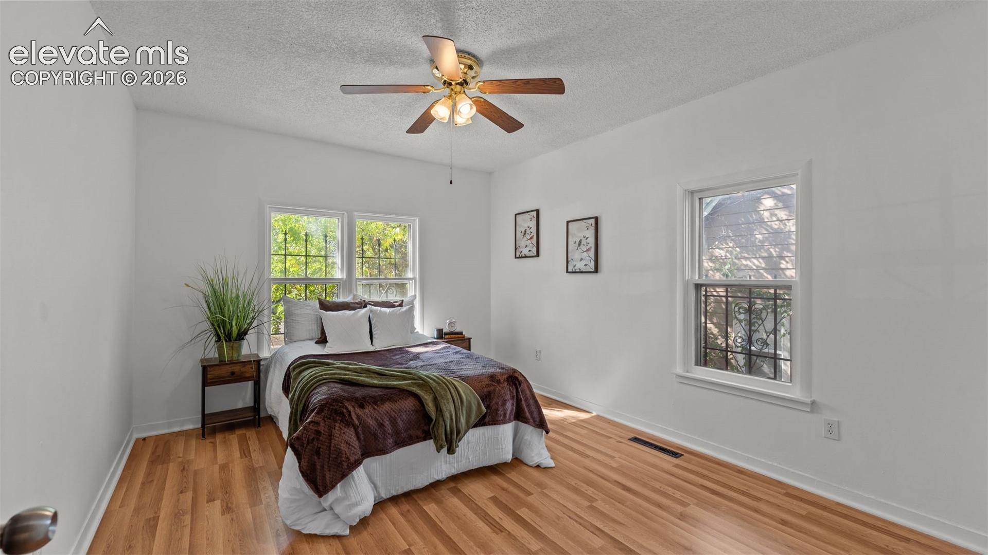 Bright secondary bedroom featuring hardwood flooring, dual windows with natural light, ceiling fan with integrated lighting, and ample square footage