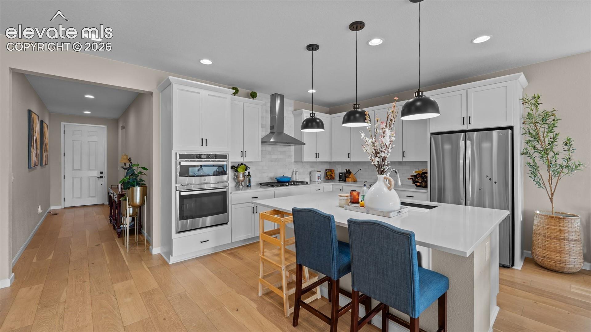 Spacious kitchen featuring an island with seating, stainless steel appliances, white cabinetry, recessed lighting, and wood-finish flooring