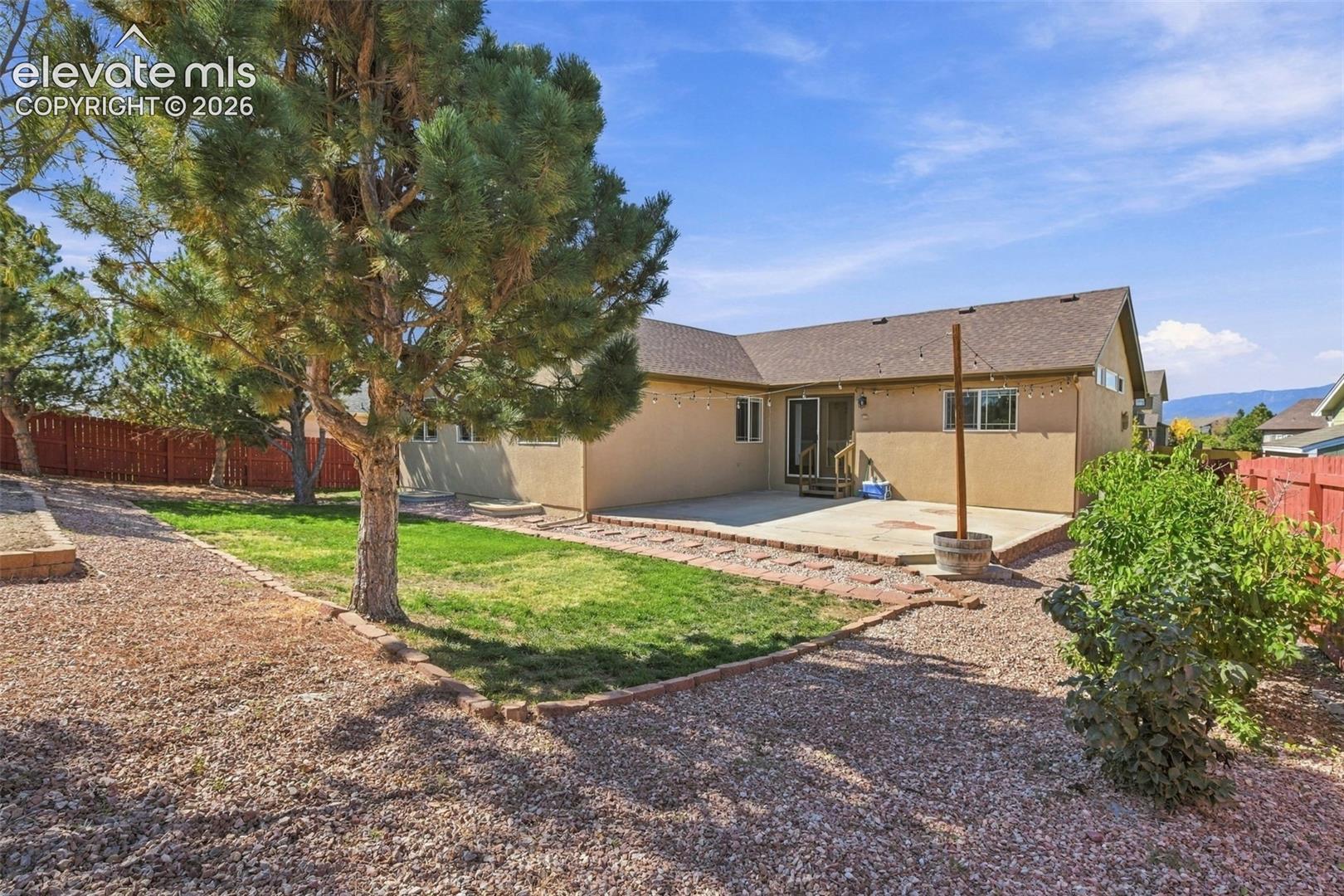 Expansive backyard featuring a concrete patio, mature trees, and a gravel perimeter