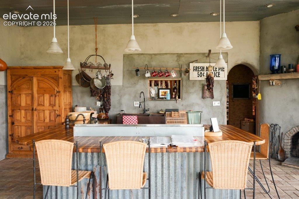 Rustic-inspired kitchen area featuring a corrugated metal island with a wood-finish countertop, pendant lighting, a built-in sink with a gooseneck faucet, an arched doorway, and a brick fireplace
