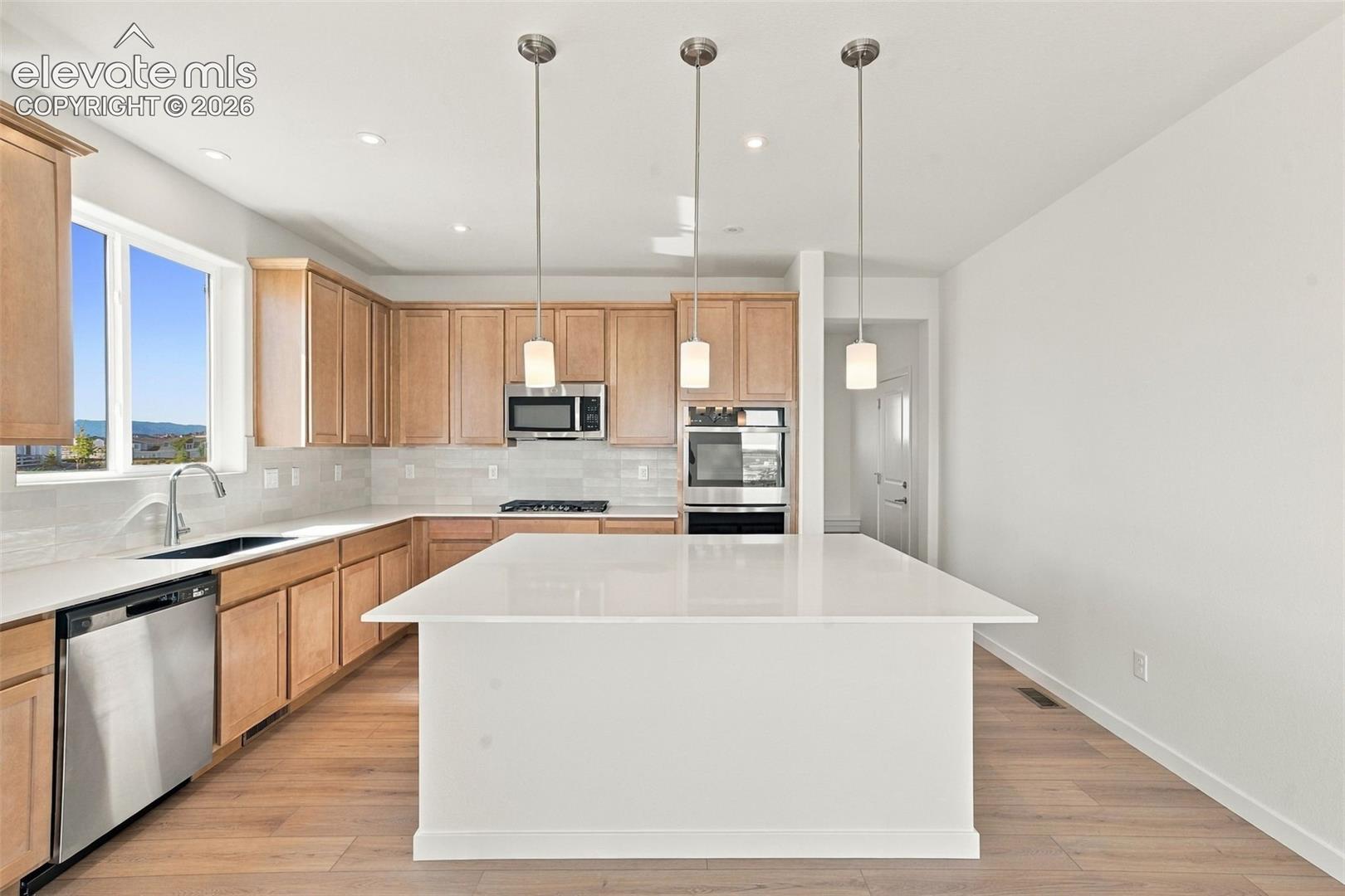 Kitchen featuring a large central island, light wood-finish cabinetry, stainless steel appliances, and a window above the sink