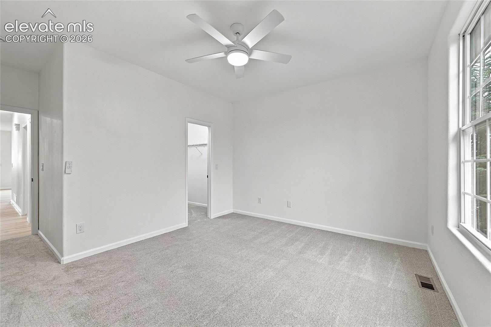 Neutral-toned wall-to-wall carpeting, multi-pane window, and a five-blade ceiling fan with integrated lighting
