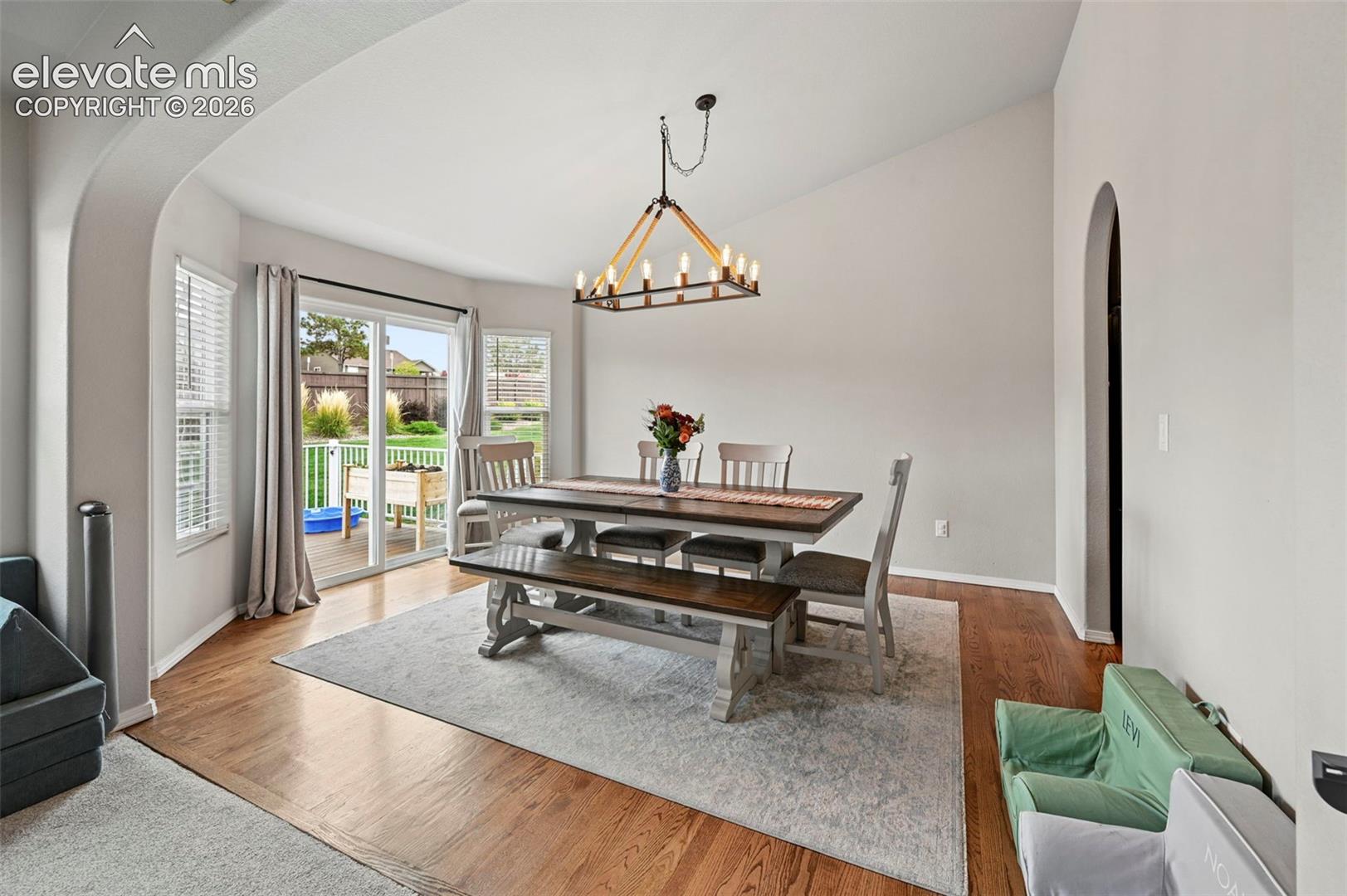 Dining area featuring vaulted ceilings, wood-finish flooring, an arched architectural opening, and a multi-light metal chandelier