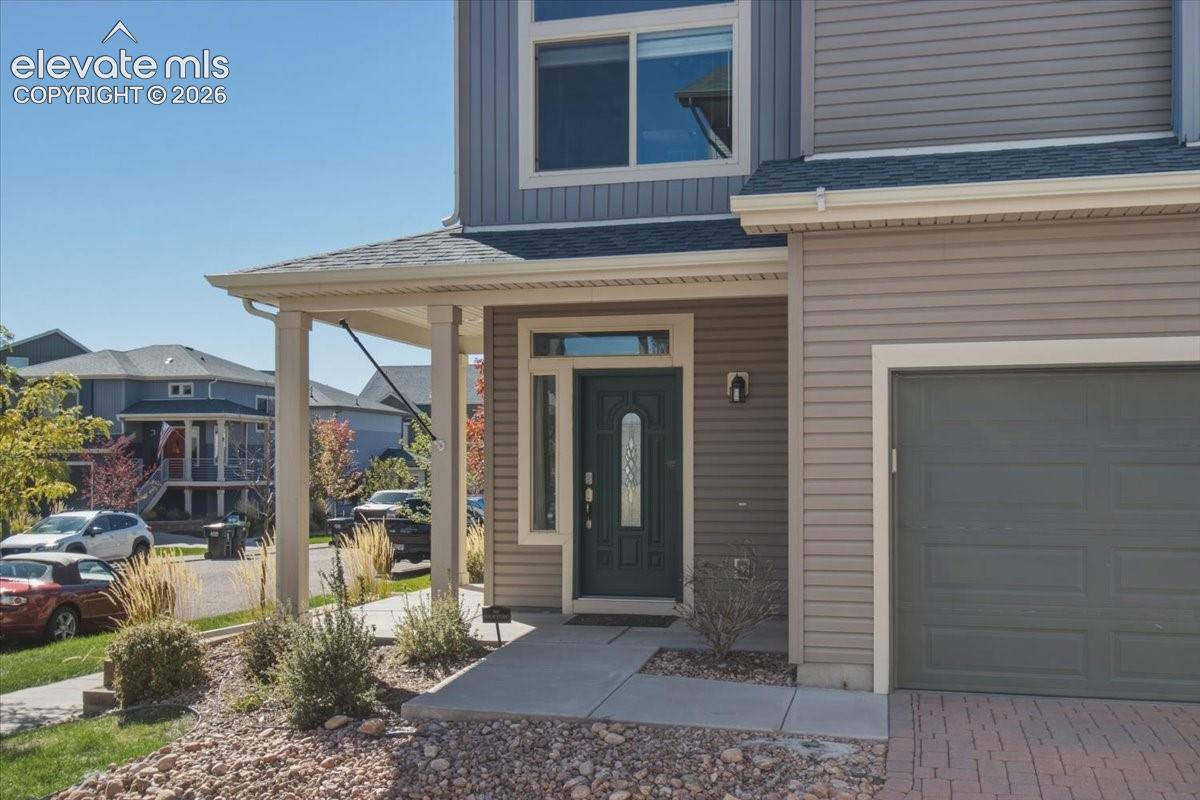 Covered entry porch, multi-pane front door, attached garage with panel door, concrete walkway, and exterior lighting fixture