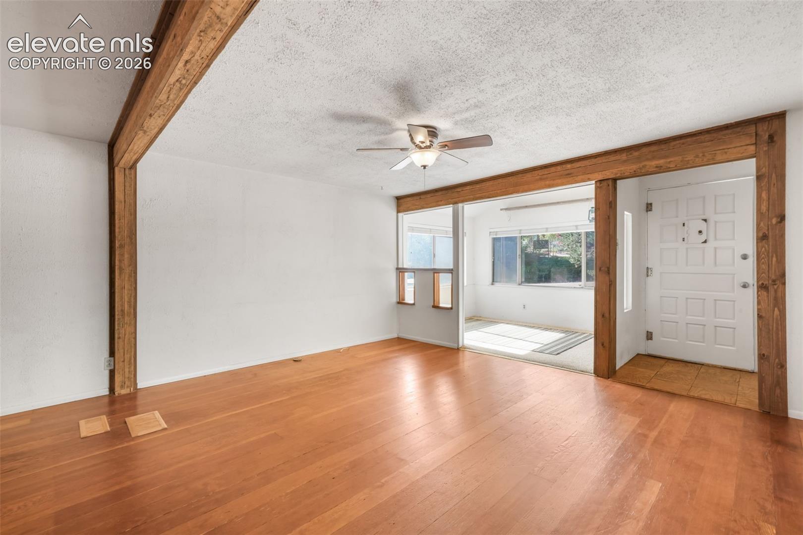 Wood-finish flooring throughout, exposed wood beams, and a ceiling fan with integrated lighting