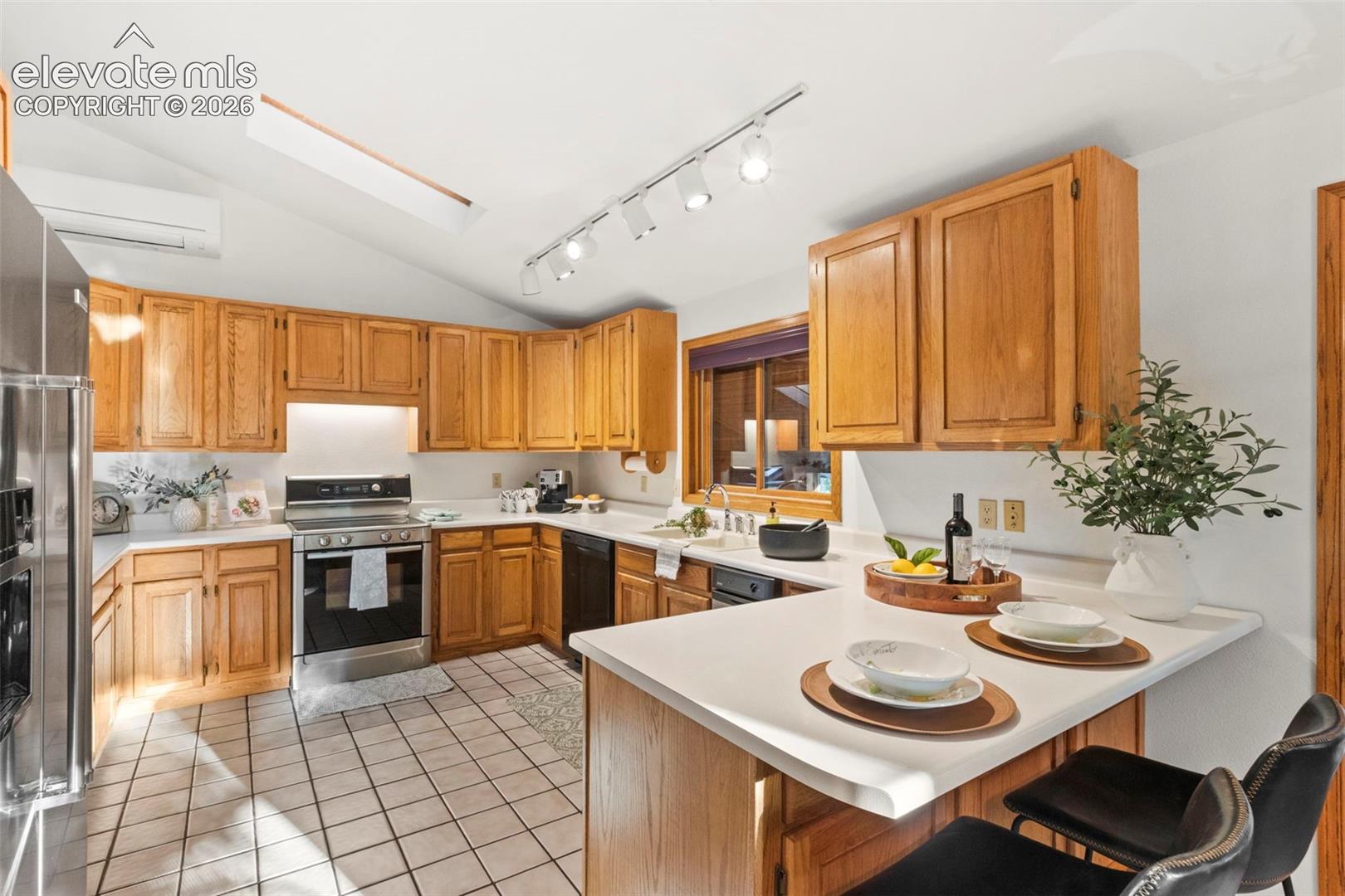 Kitchen featuring wood cabinetry, solid-surface countertops, tile flooring, track lighting, and a vaulted ceiling with a skylight