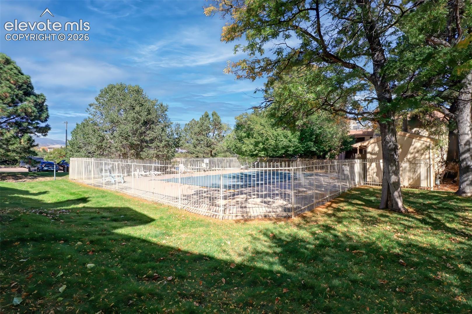 Community swimming pool with metal perimeter fencing and mature landscaping. 