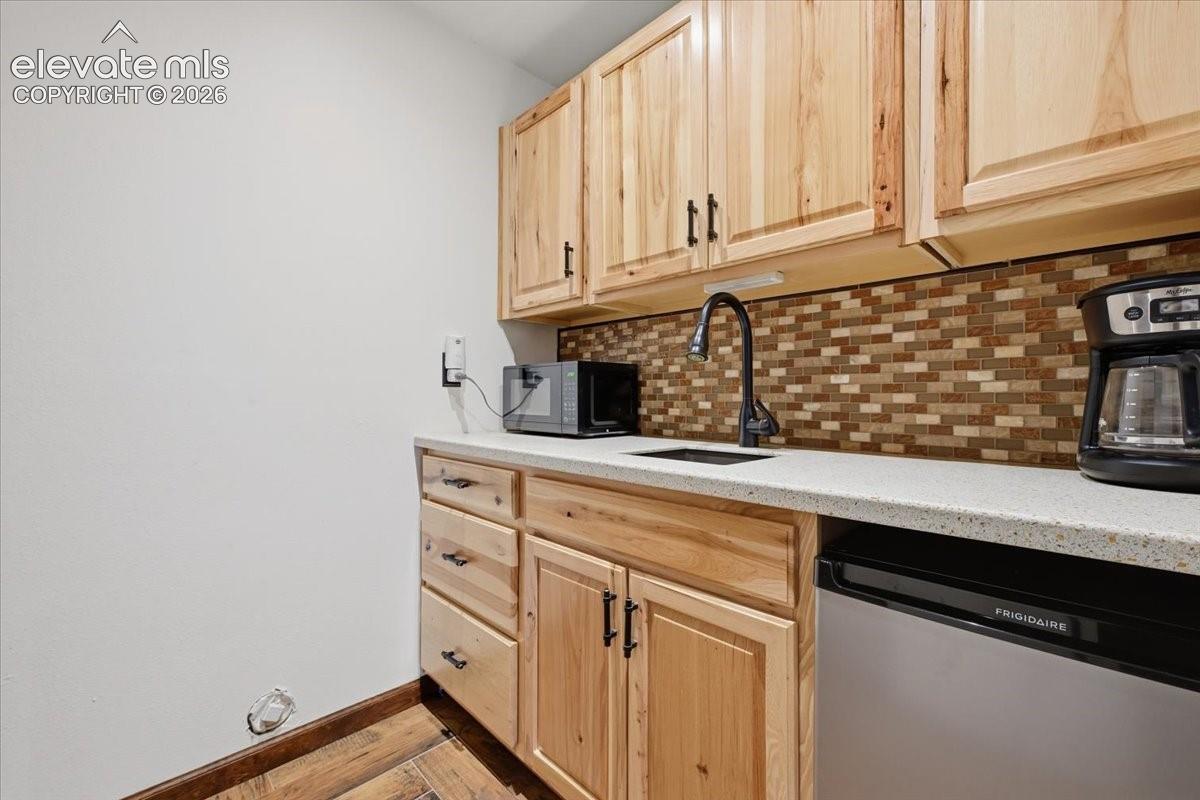 Wood-finish cabinetry with dark hardware, stone-finish countertop, mosaic tile backsplash, integrated compact refrigerator, and wood-finish flooring