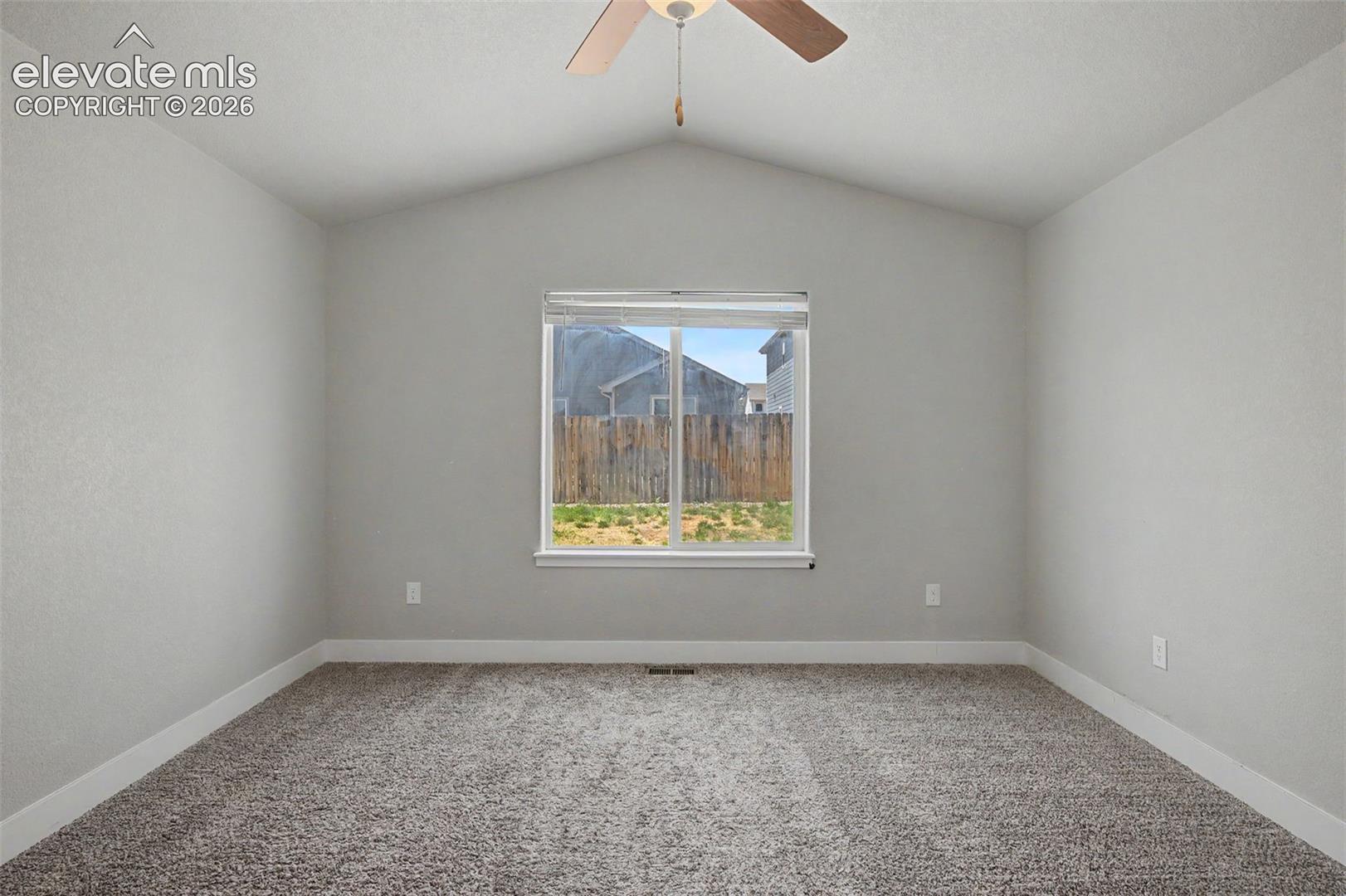 Bright bedroom featuring vaulted ceilings, a central window, neutral carpeting, and a ceiling fan