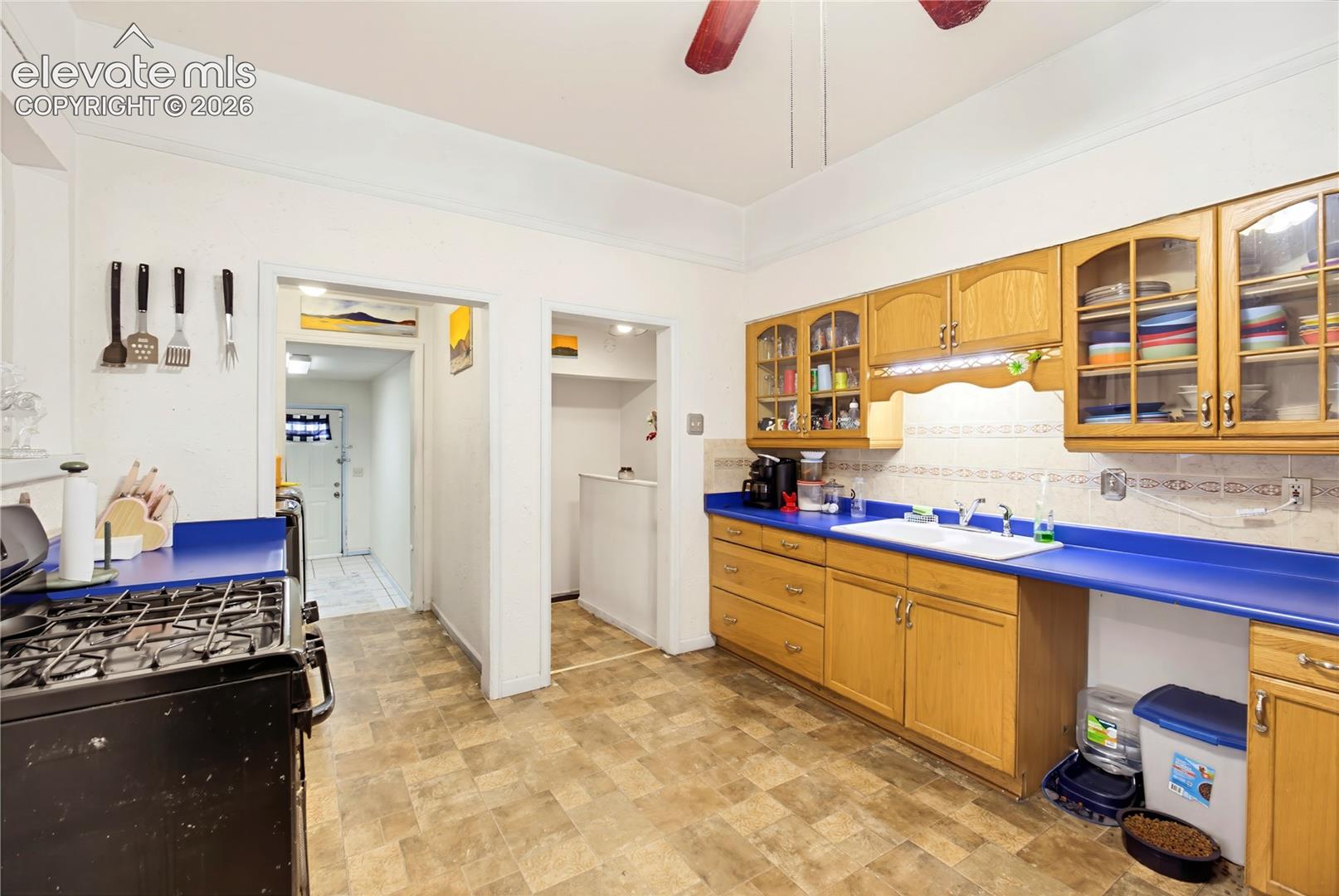 Kitchen featuring wood-finish cabinetry, a gas range, dual-basin sink, and a patterned backsplash