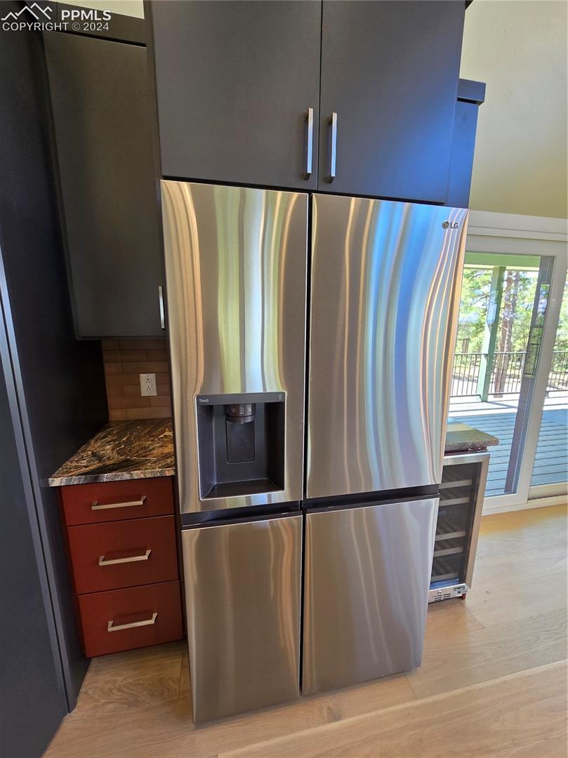 Kitchen with dark stone countertops, stainless steel refrigerator with ice dispenser, decorative backsplash, and light hardwood / wood-style flooring