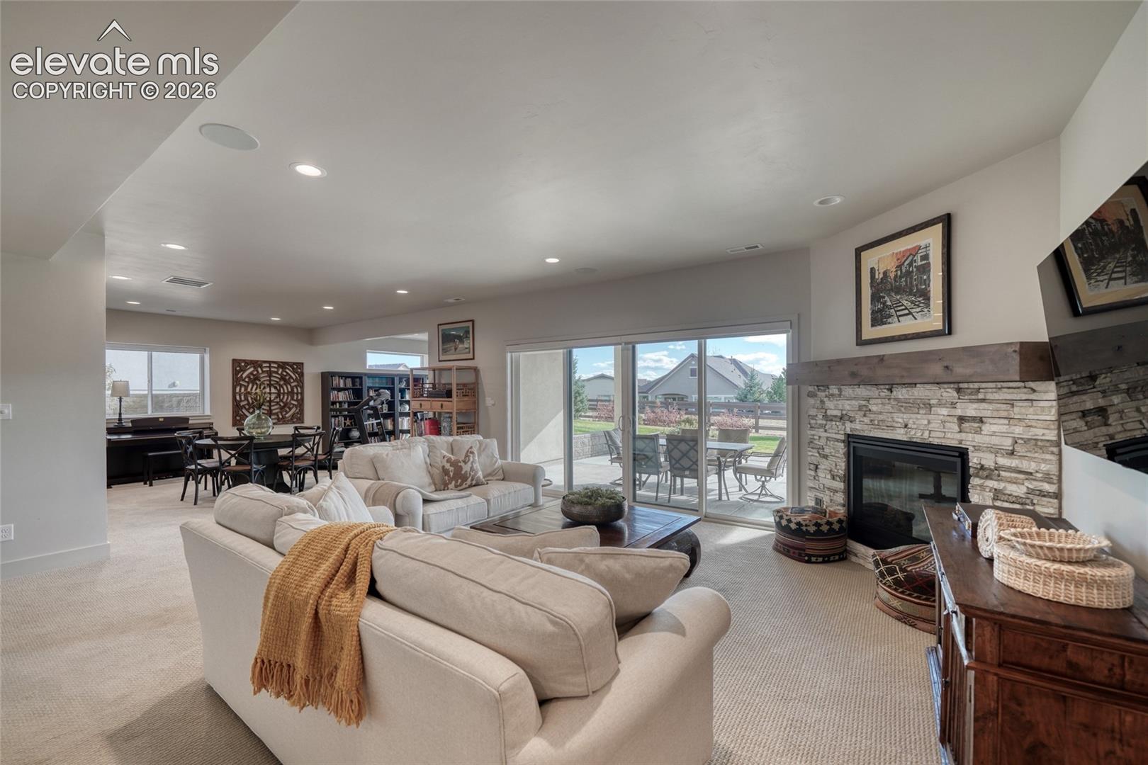 Open living area featuring a floor-to-ceiling stone fireplace with a natural wood mantel, recessed lighting, and expansive sliding glass doors