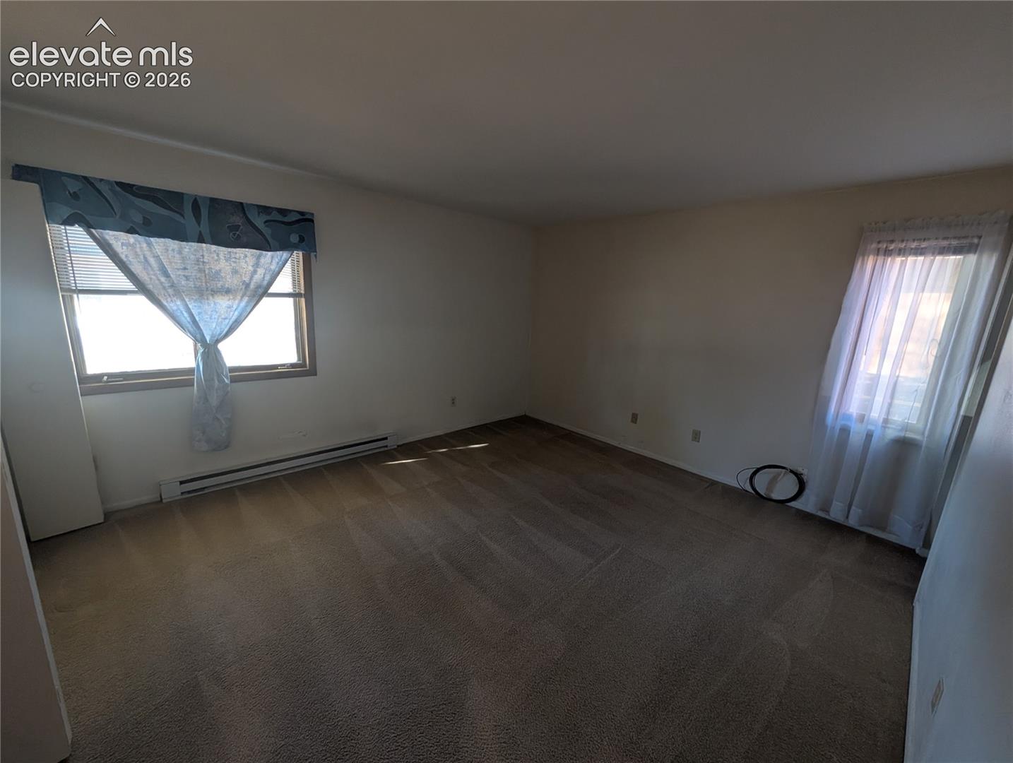 Carpeted interior space with multiple windows and baseboard heating