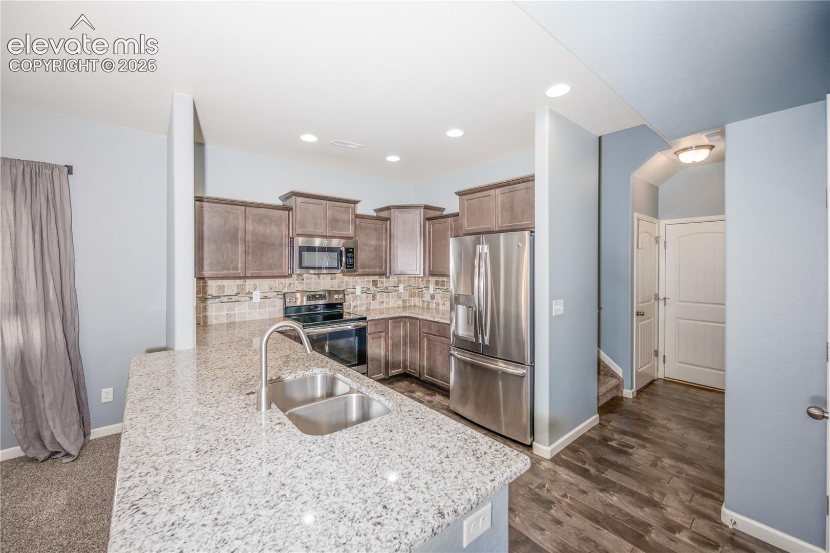 Kitchen featuring a spacious peninsula with stone-finish countertops, stainless steel appliances, wood-finish cabinetry, and recessed lighting