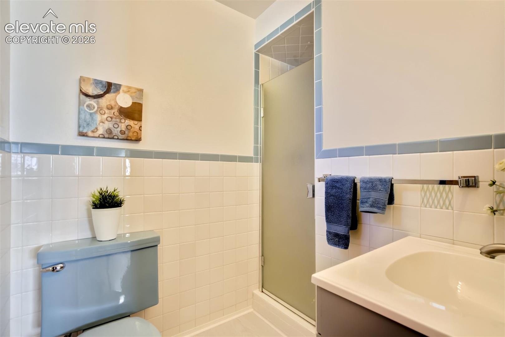 Bathroom featuring a vanity with integrated sink, shower enclosure with frosted glass door, and white wall tile with blue accent trim