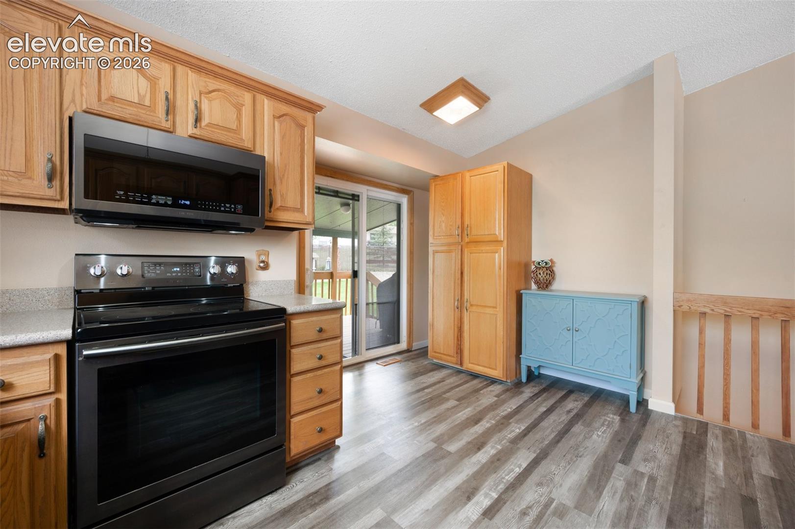 Kitchen with black / electric stove, stainless steel microwave, light wood-type flooring, and light countertops