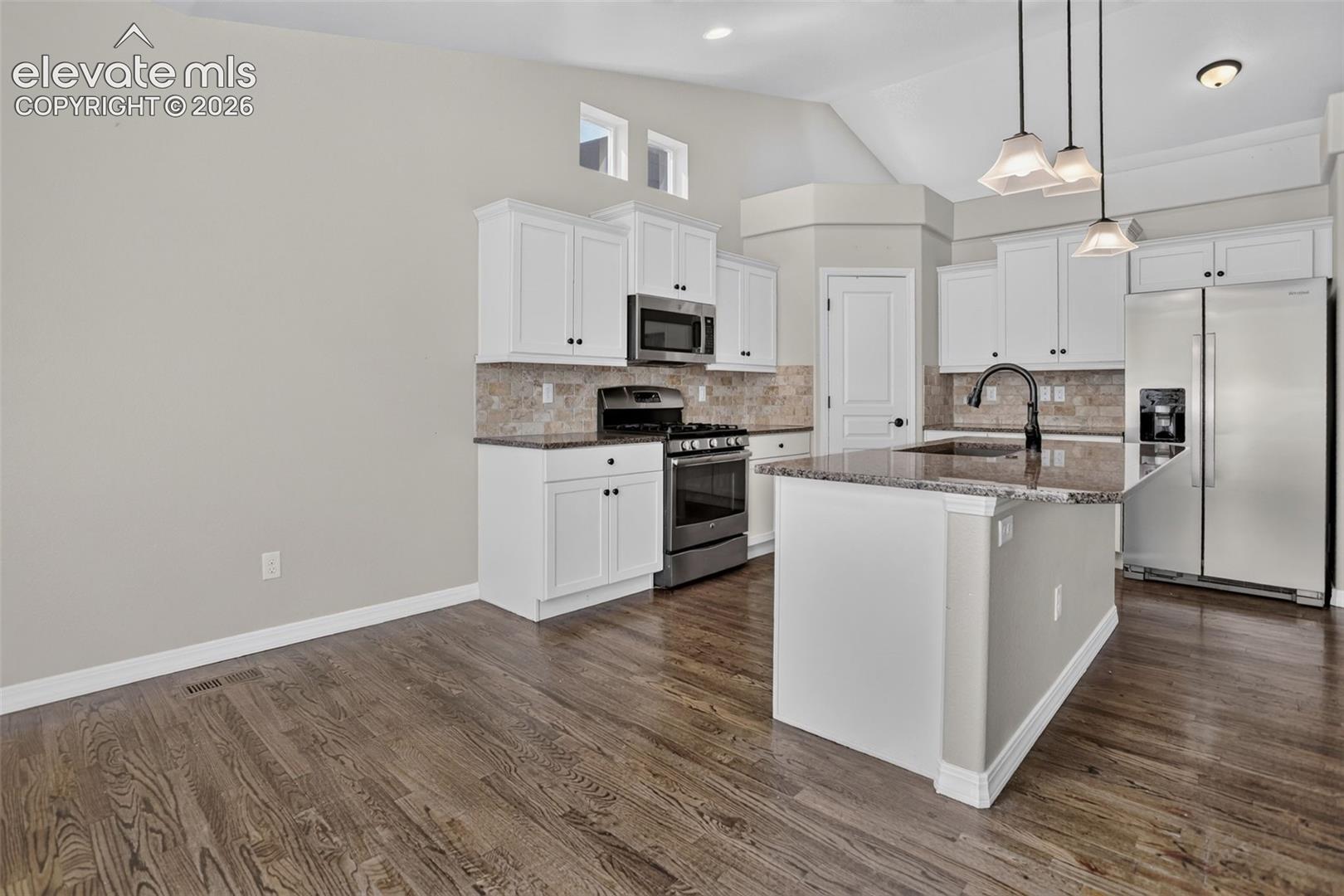 Kitchen featuring wood-finish flooring, white cabinetry, a central island with a stone countertop, stainless steel appliances, and a tiled backsplash