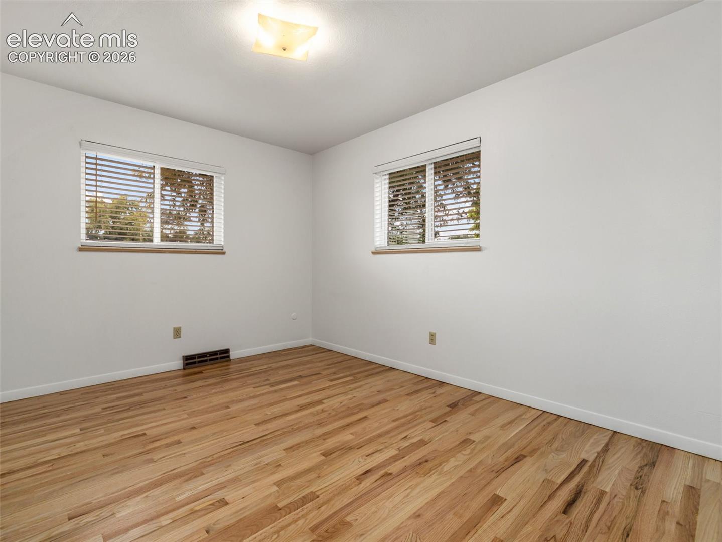 Two windows with blinds, wood-finish flooring, and a ceiling-mounted light fixture