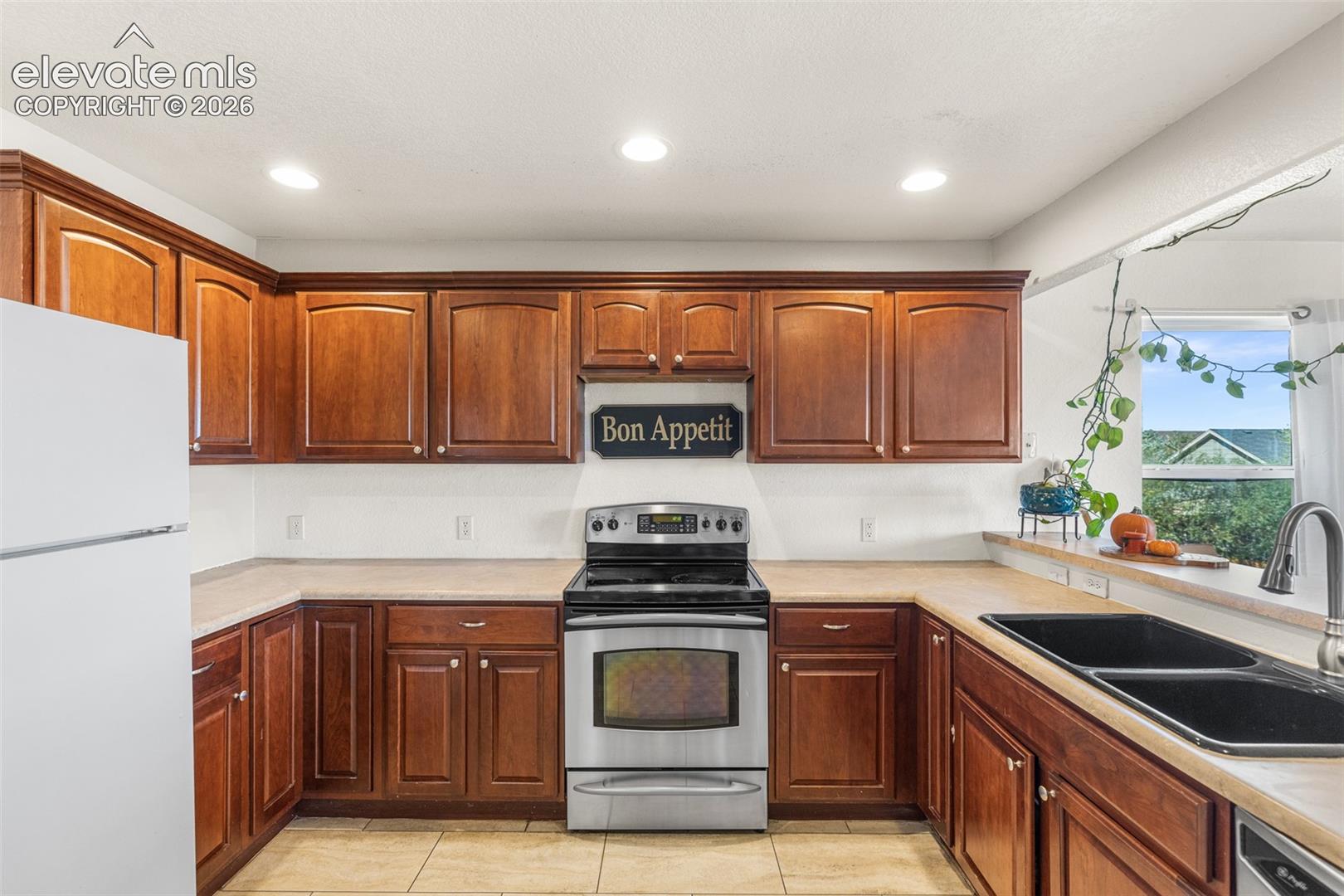 Kitchen featuring medium-tone wood cabinetry, recessed lighting, stainless steel oven, matte black double-basin sink, and tile flooring