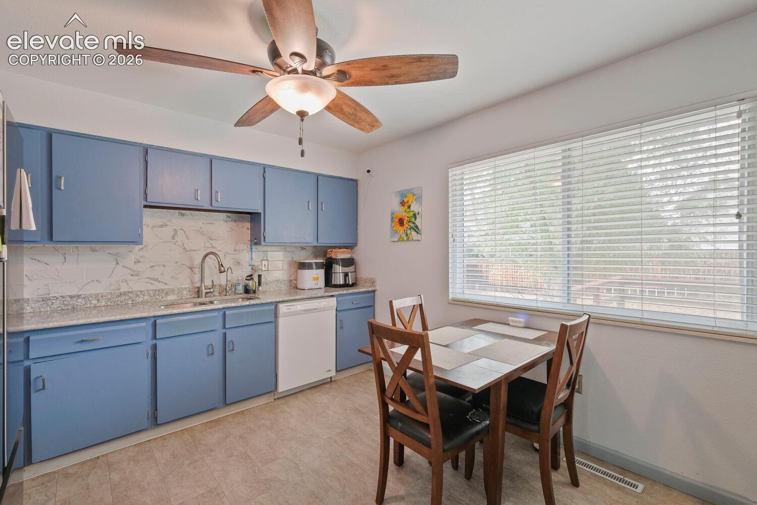 Kitchen featuring blue cabinetry, light-toned countertops, tile backsplash, and a ceiling fan with integrated lighting