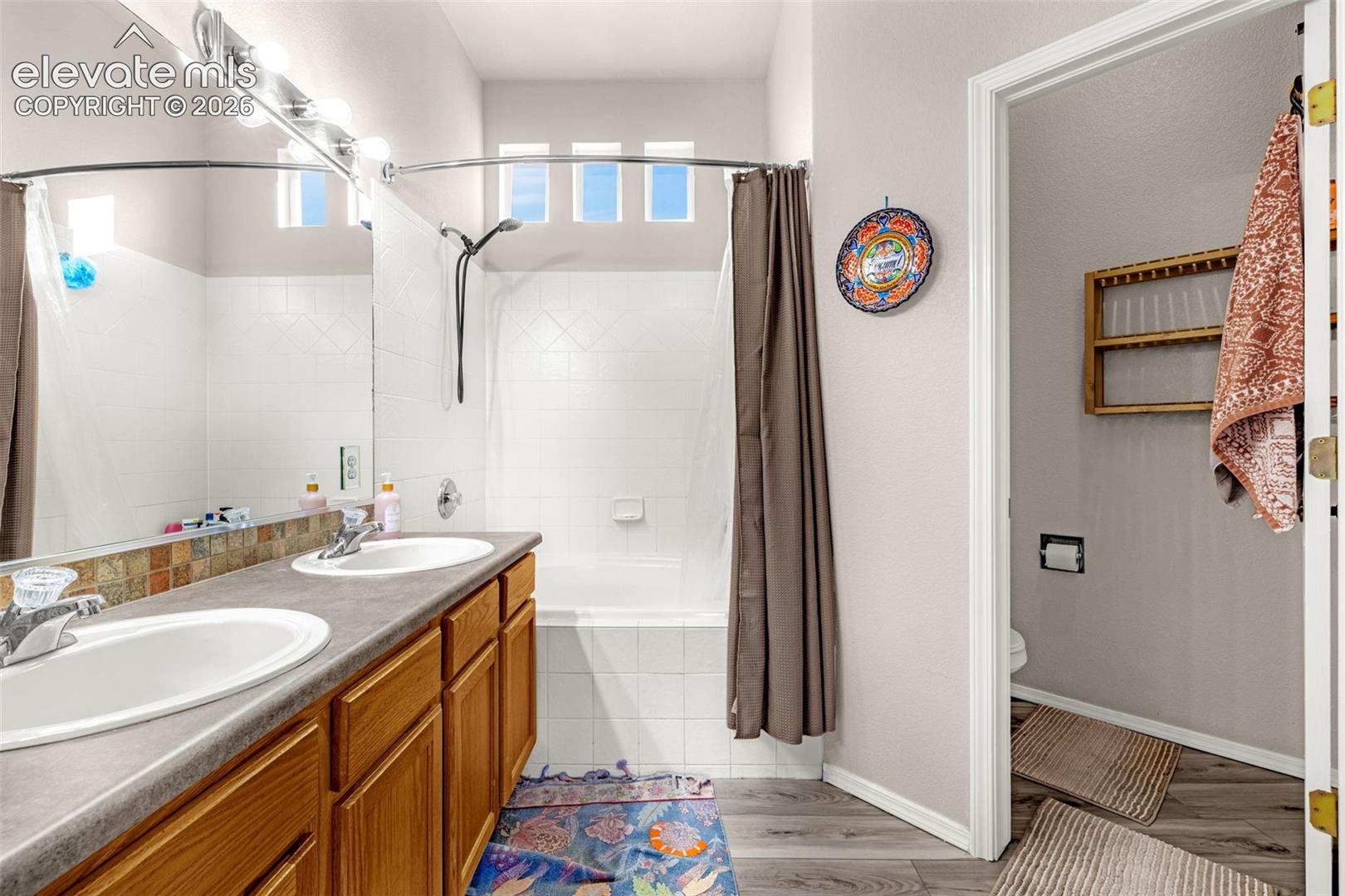 Bathroom featuring a dual-sink vanity with wood-finish cabinetry, a full-width vanity mirror, a combination tub and shower with tile surround, and three transom windows