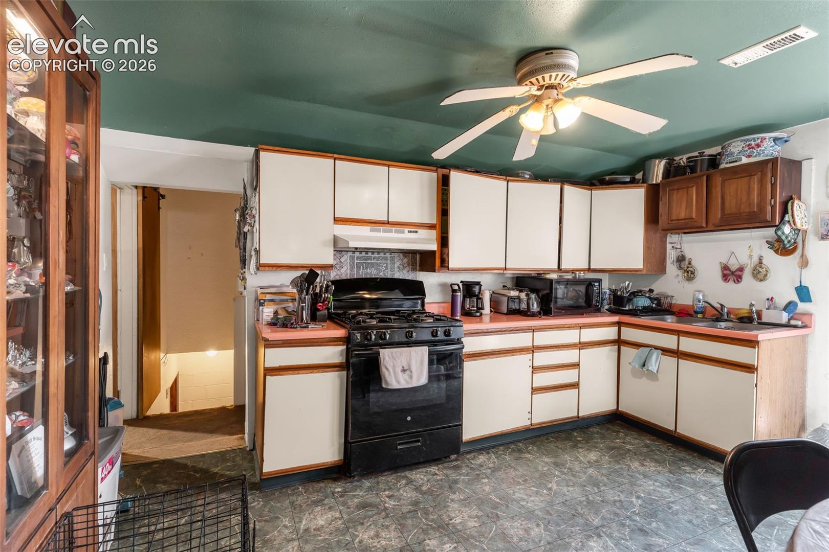 Kitchen featuring L-shaped cabinetry, a built-in range, a single basin sink, and an overhead ceiling fan