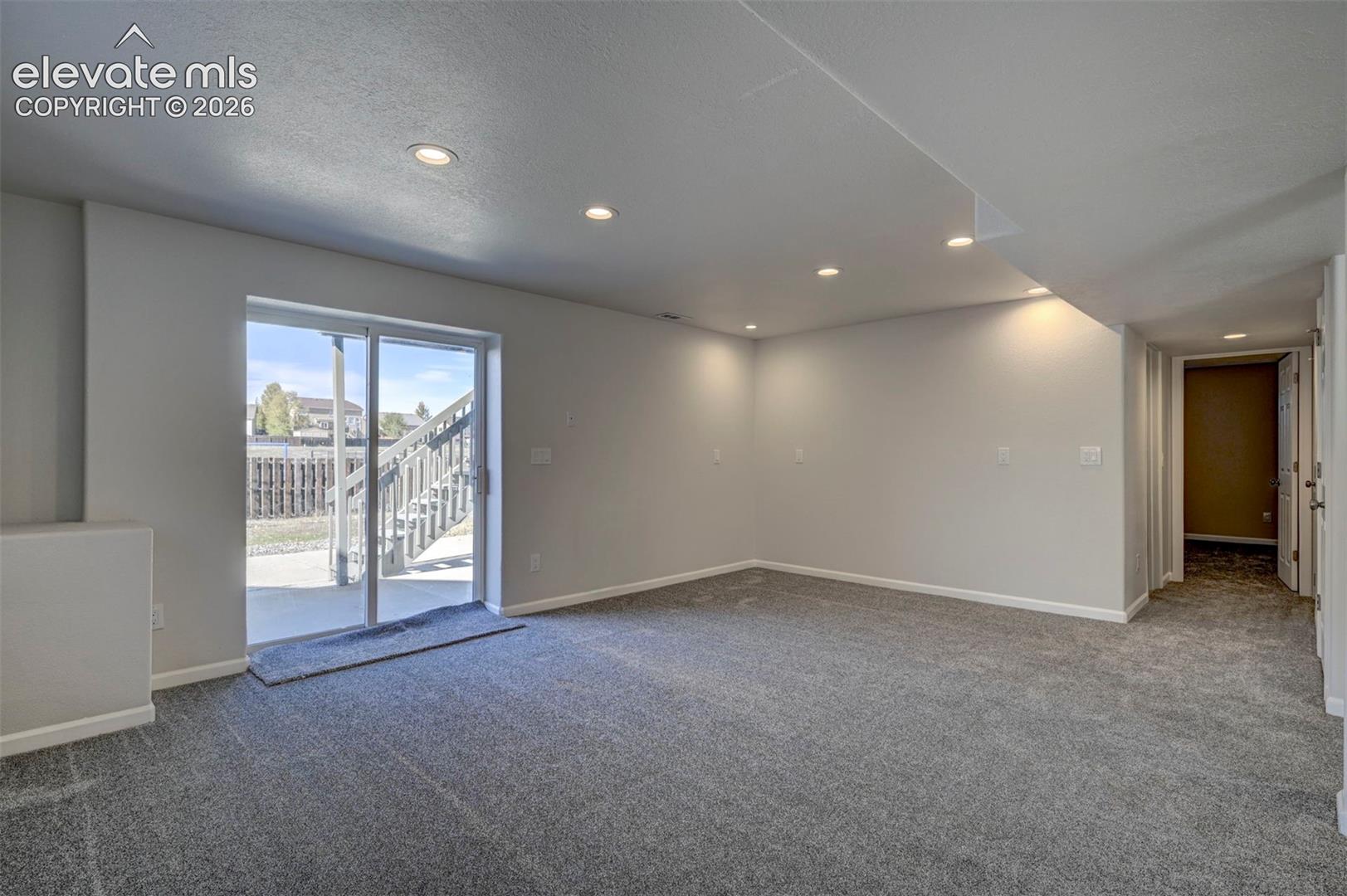 Neutral-toned interior space featuring recessed ceiling lighting, wall-to-wall carpeting, and a glass sliding door providing exterior access